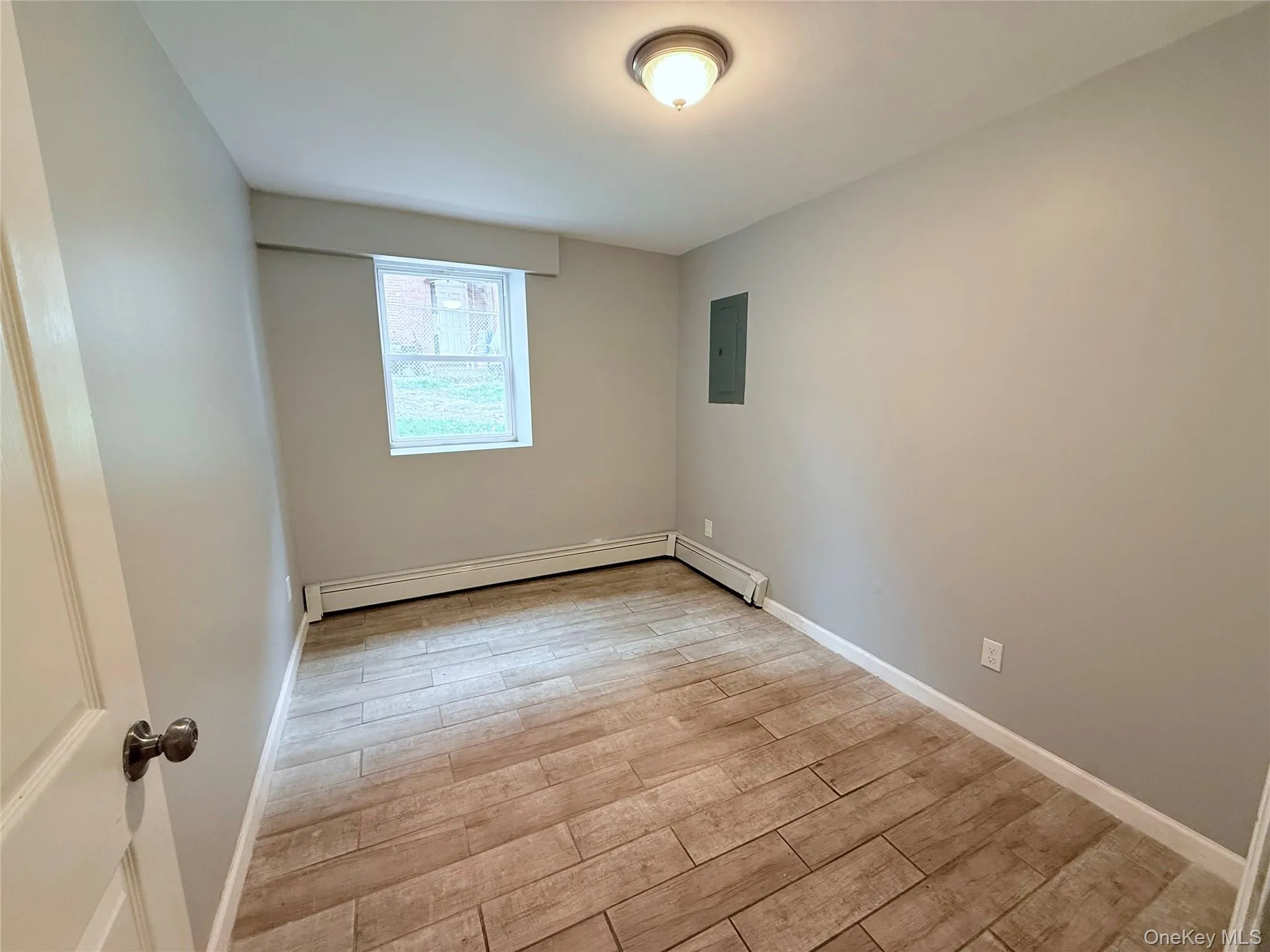 Unfurnished room with light wood-style floors, electric panel, and a baseboard radiator Unfurnished room with light wood-style floors, electric panel, and a baseboard radiator