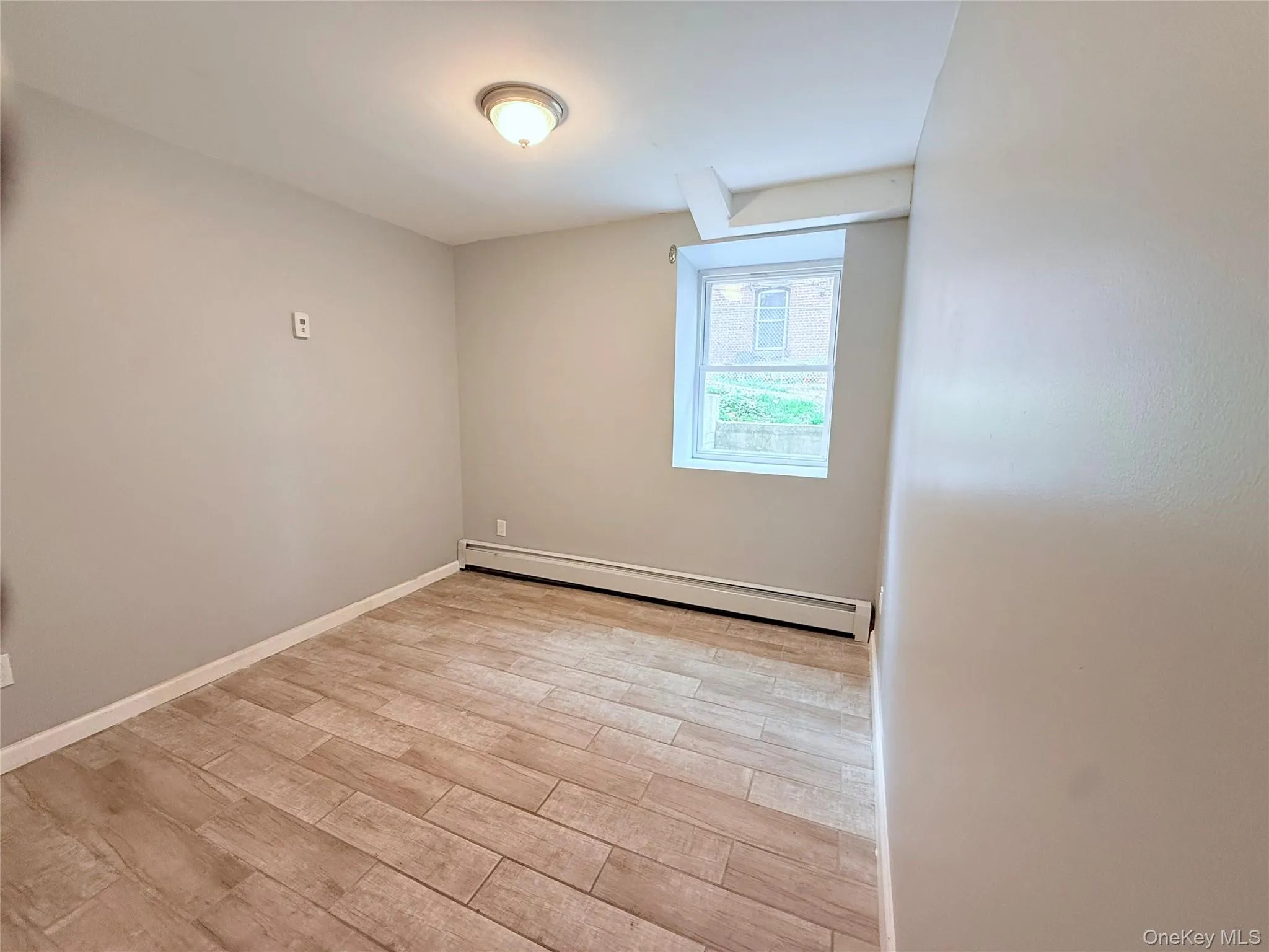 Unfurnished room with baseboard heating and light wood-style floors Unfurnished room with baseboard heating and light wood-style floors