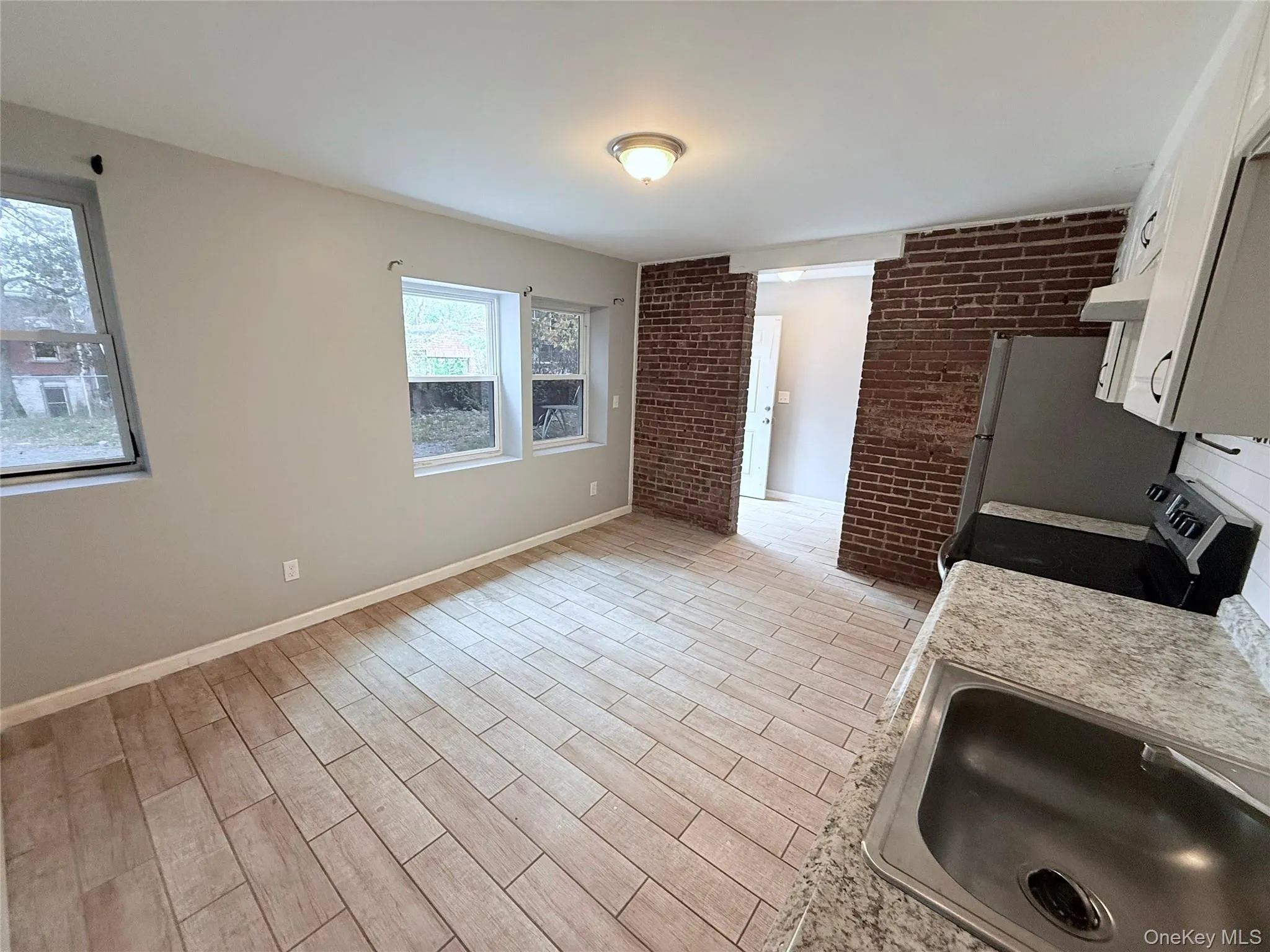 Kitchen featuring white cabinets, light wood-style floors, light countertops, brick wall, and stainless steel electric range Kitchen featuring white cabinets, light wood-style floors, light countertops, brick wall, and stainless steel electric range