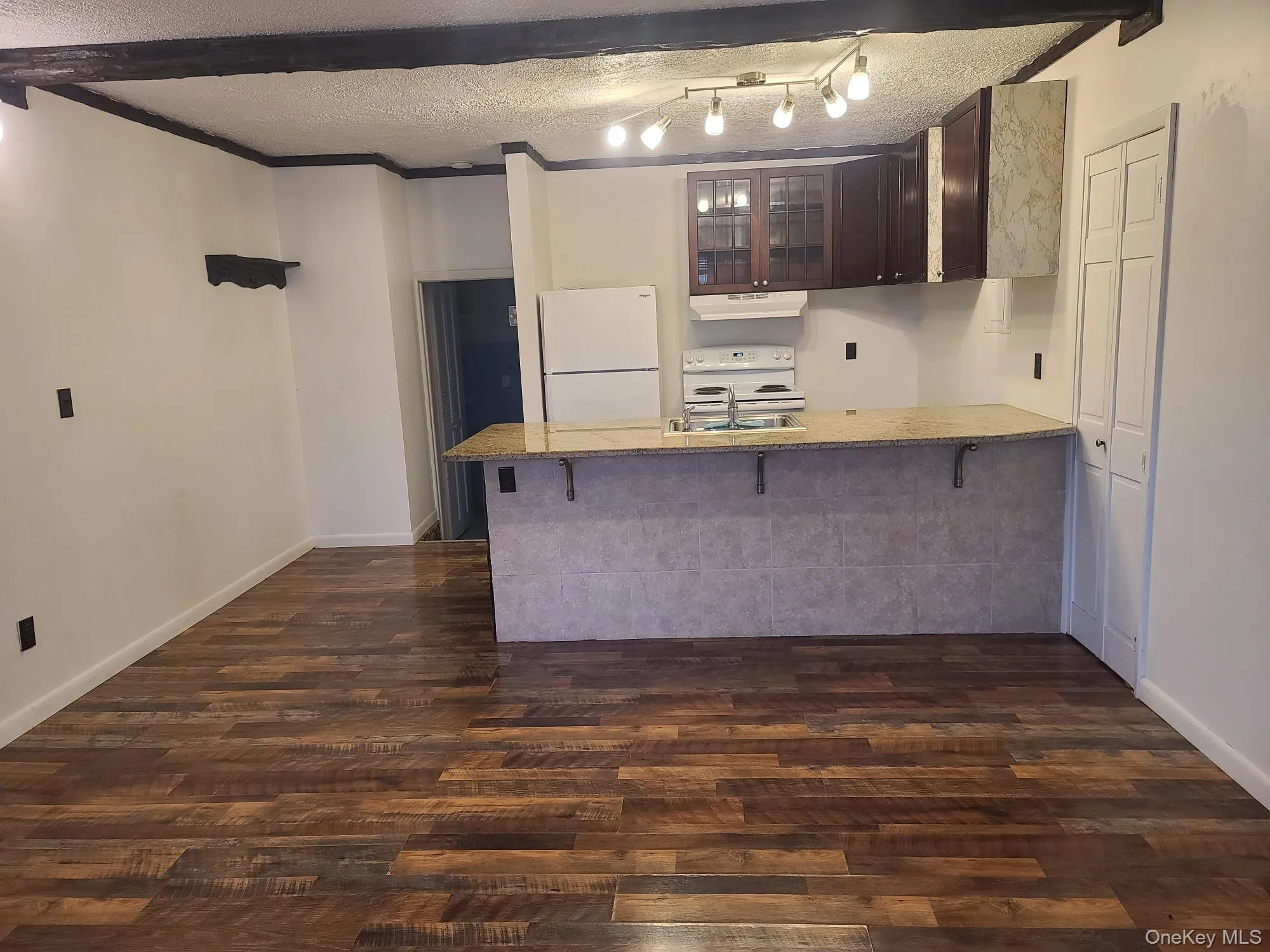 Kitchen cabinets, a textured ceiling, a counter bar, white appliances, and dark brown cabinetry Kitchen cabinets, a textured ceiling, a counter bar, white appliances, and dark brown cabinetry