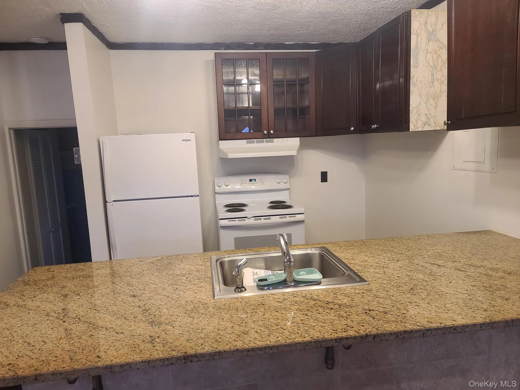 Kitchen with dark brown cabinets, white appliances, cabinets, under cabinet range hood Kitchen with dark brown cabinets, white appliances, cabinets, under cabinet range hood