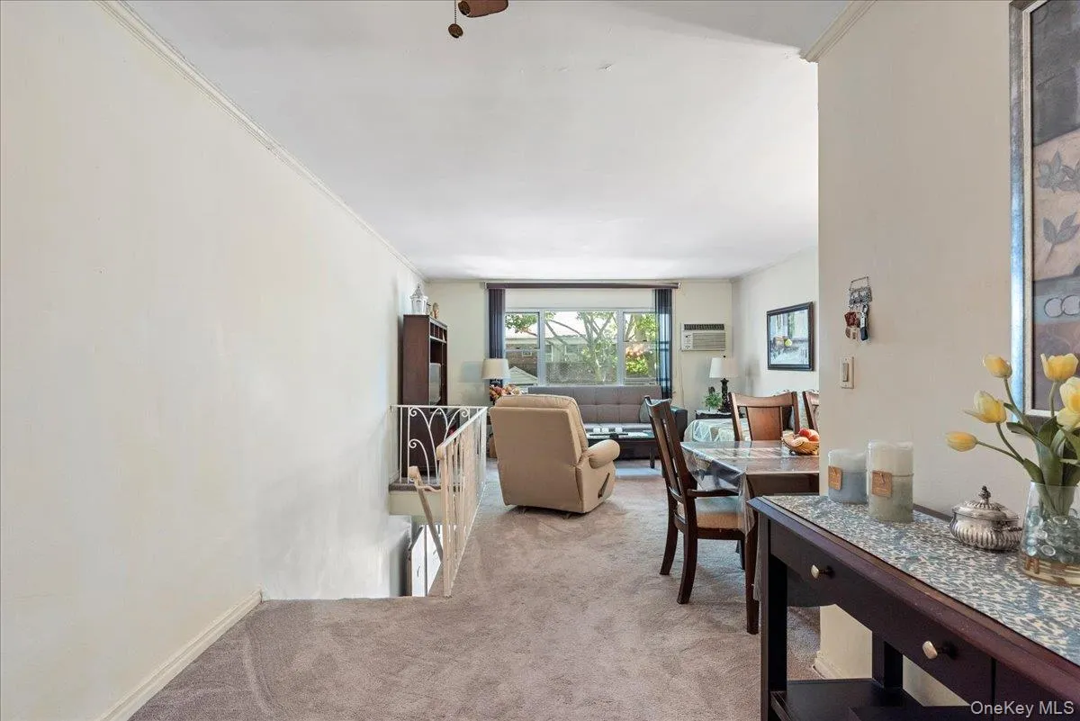Living area featuring crown molding, light colored carpet, and a wall unit AC Living area featuring crown molding, light colored carpet, and a wall unit AC