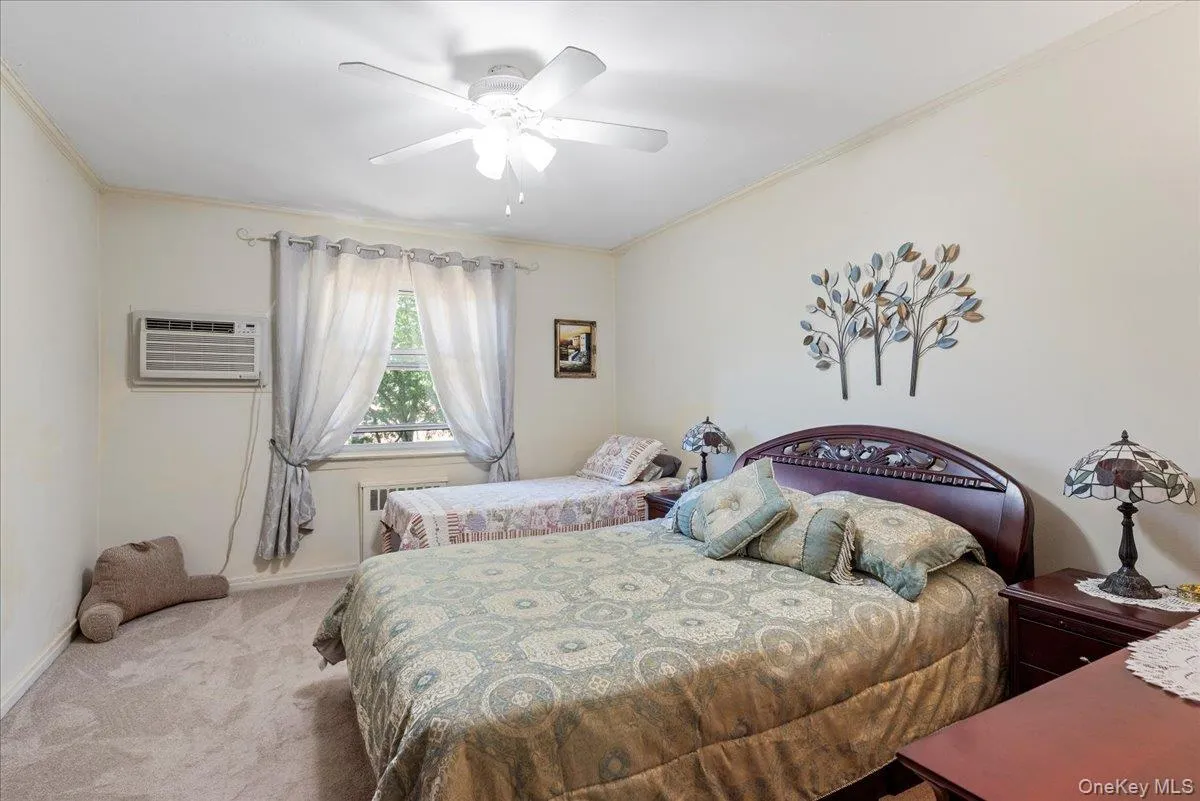 Bedroom featuring ornamental molding, carpet floors, ceiling fan, an AC wall unit, and radiator heating unit Bedroom featuring ornamental molding, carpet floors, ceiling fan, an AC wall unit, and radiator heating unit