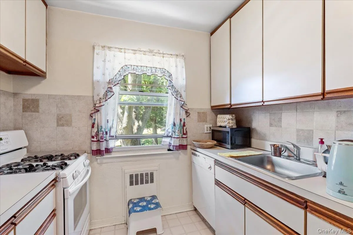 Kitchen with white appliances, white cabinetry, light countertops, brown cabinets, and radiator Kitchen with white appliances, white cabinetry, light countertops, brown cabinets, and radiator