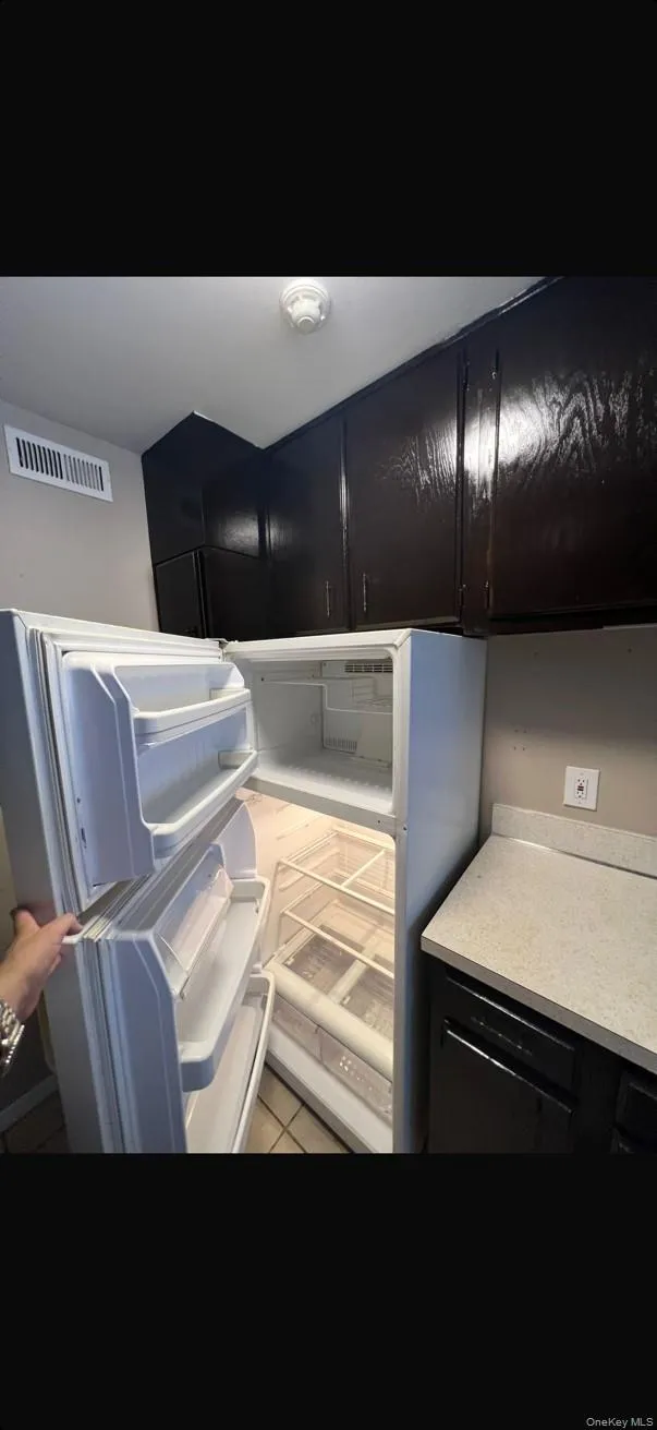 Kitchen with dark cabinets, light countertops, fridge, and light tile patterned floors Kitchen with dark cabinets, light countertops, fridge, and light tile patterned floors