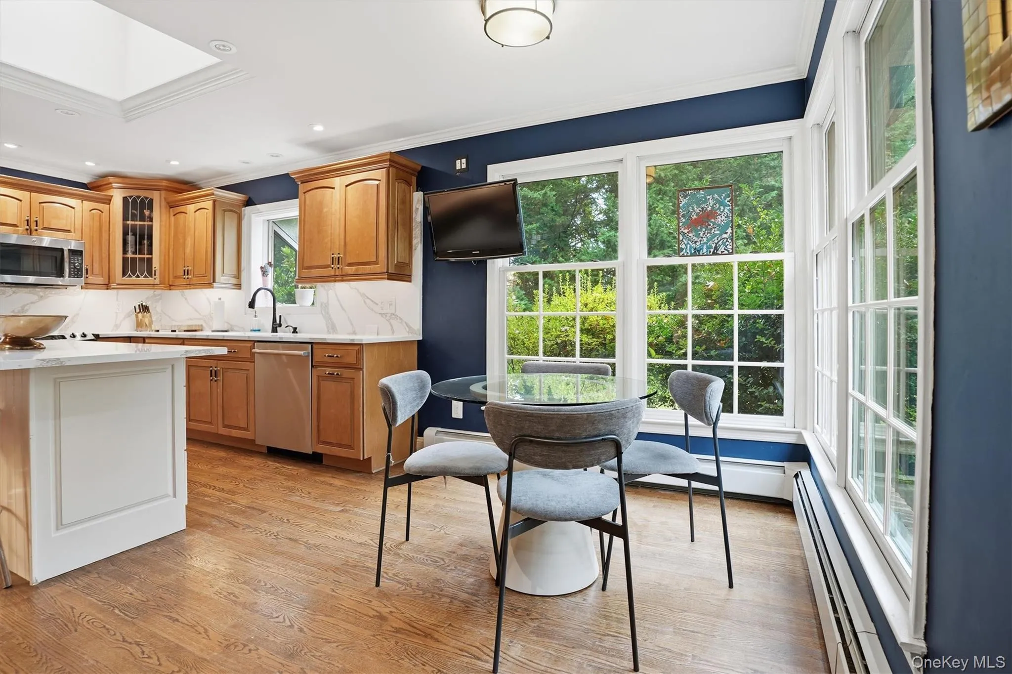 Kitchen featuring ornamental molding, light wood-style flooring, brown cabinetry, backsplash, and glass insert cabinets Kitchen featuring ornamental molding, light wood-style flooring, brown cabinetry, backsplash, and glass insert cabinets