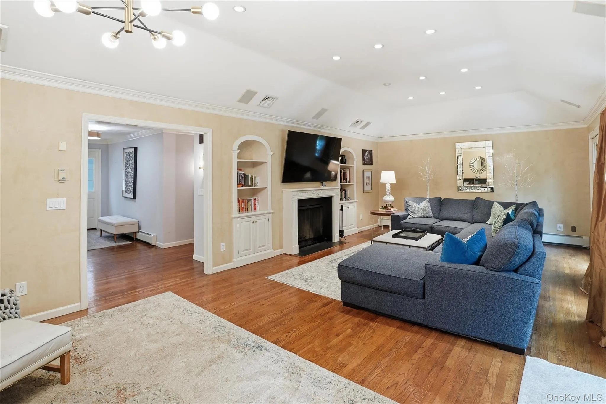 Living room with a fireplace with flush hearth, light wood finished floors, crown molding, and built in features Living room with a fireplace with flush hearth, light wood finished floors, crown molding, and built in features