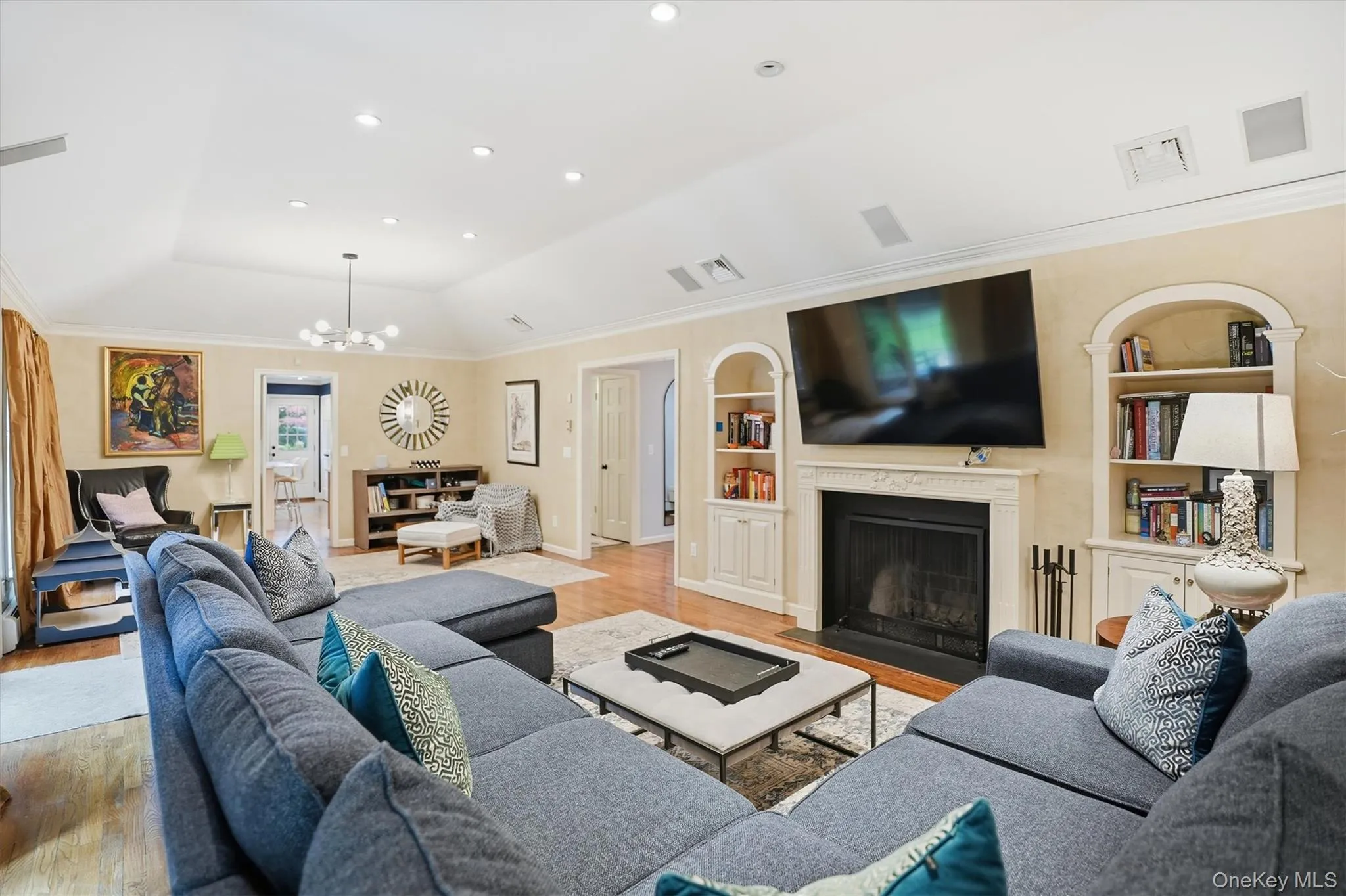 Living area with light wood finished floors, a fireplace with flush hearth, built in shelves, recessed lighting, and ornamental molding Living area with light wood finished floors, a fireplace with flush hearth, built in shelves, recessed lighting, and ornamental molding