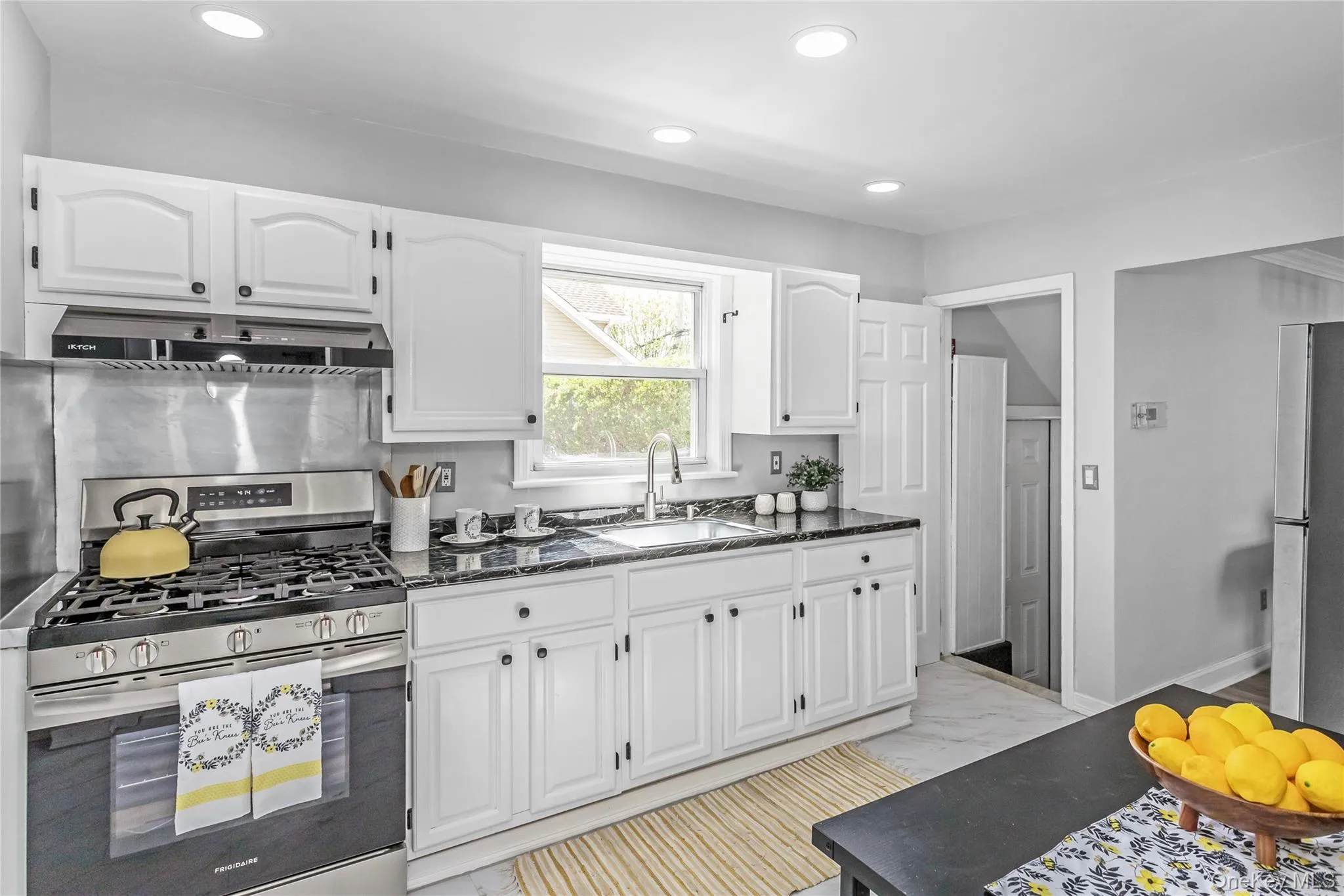 Kitchen featuring marble finish floor, under cabinet range hood, white cabinets, a sink, and stainless steel appliances Kitchen featuring marble finish floor, under cabinet range hood, white cabinets, a sink, and stainless steel appliances