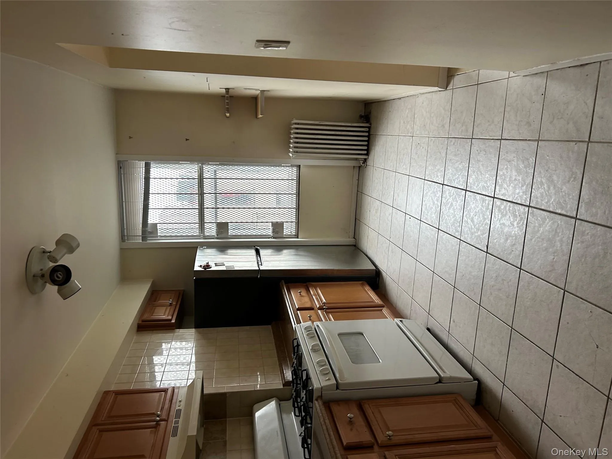 Kitchen featuring range, dark countertops, brown cabinetry, radiator, and light tile patterned flooring Kitchen featuring range, dark countertops, brown cabinetry, radiator, and light tile patterned flooring