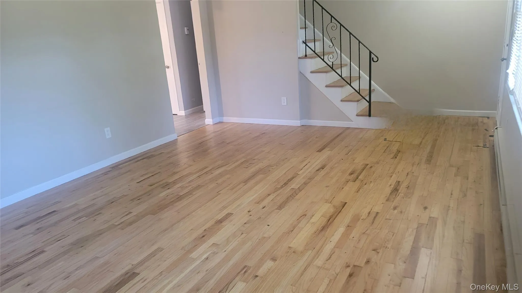 Unfurnished living room featuring light wood-type flooring, stairs, and a baseboard heating unit Unfurnished living room featuring light wood-type flooring, stairs, and a baseboard heating unit