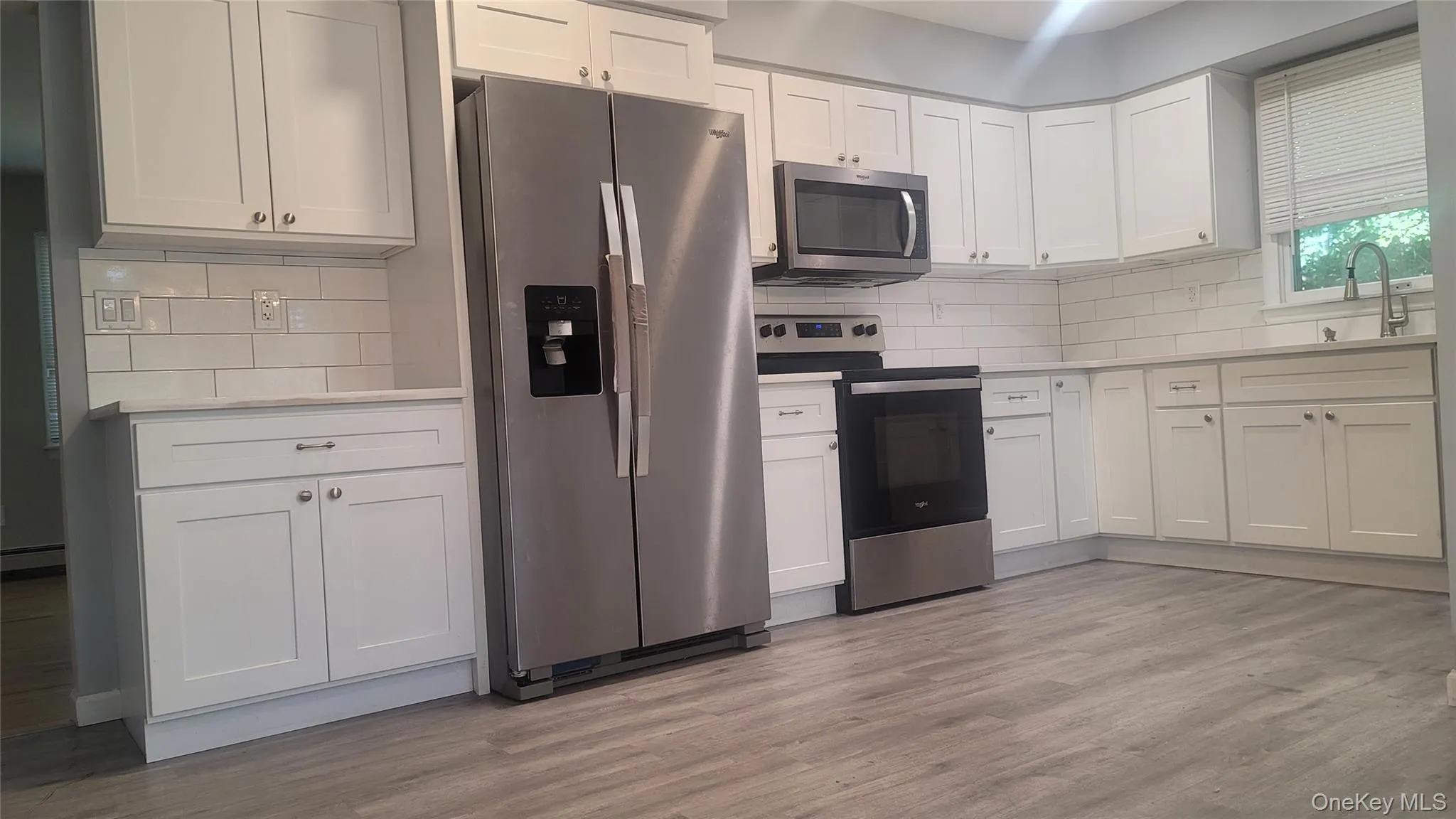 Kitchen with appliances with stainless steel finishes, white cabinets, tasteful backsplash, light wood-type flooring, and a baseboard radiator Kitchen with appliances with stainless steel finishes, white cabinets, tasteful backsplash, light wood-type flooring, and a baseboard radiator