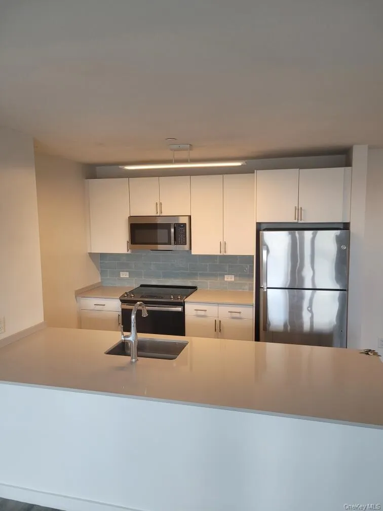 Kitchen with appliances with stainless steel finishes, backsplash, white cabinetry, a peninsula, and light stone countertops Kitchen with appliances with stainless steel finishes, backsplash, white cabinetry, a peninsula, and light stone countertops