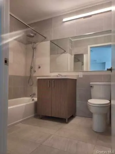 Full bath featuring vanity, tile walls, tub / shower combination, and light tile patterned flooring Full bath featuring vanity, tile walls, tub / shower combination, and light tile patterned flooring