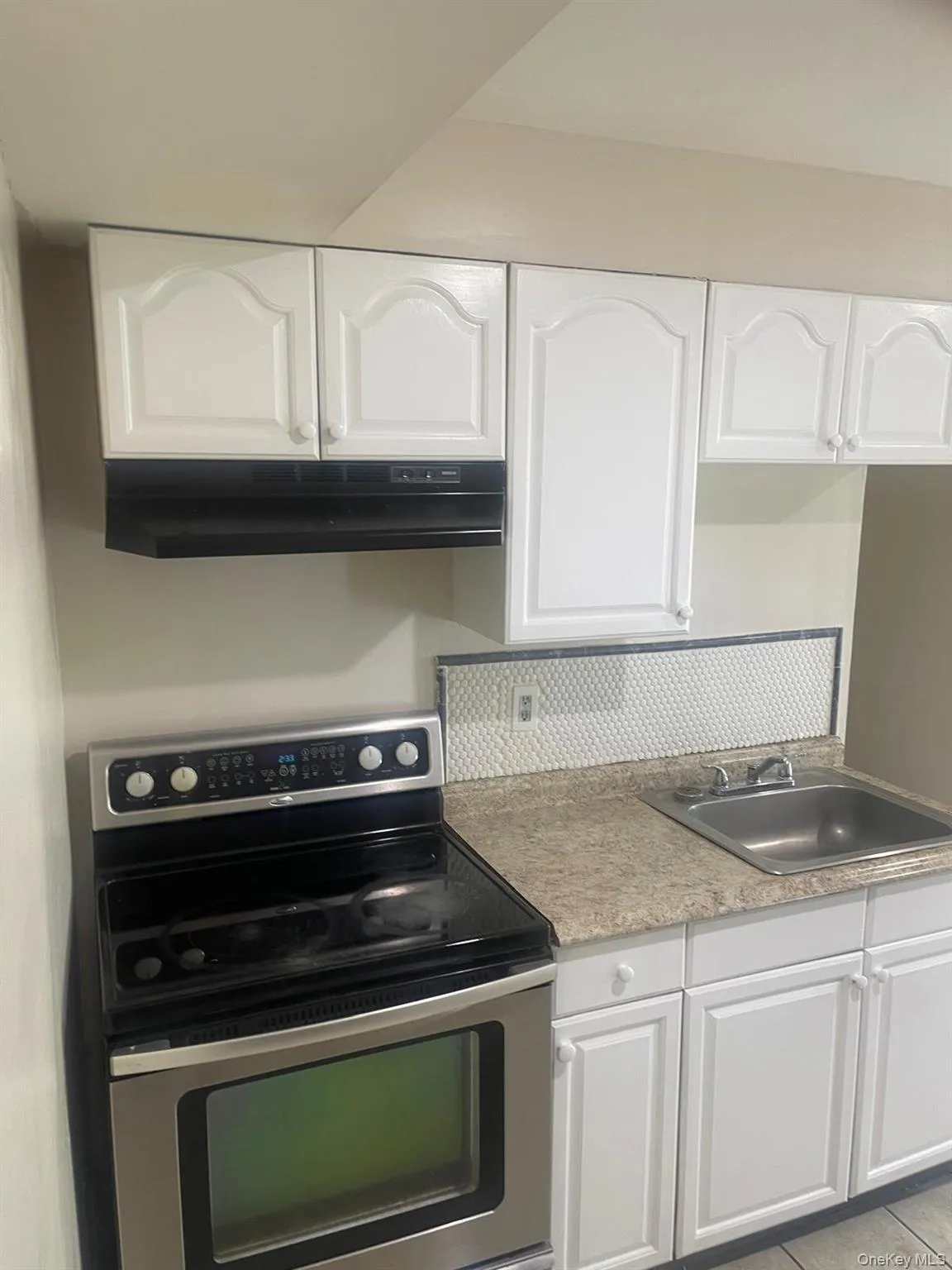 Kitchen featuring stainless steel range with electric stovetop, white cabinets, under cabinet range hood, light tile patterned floors, and light countertops Kitchen featuring stainless steel range with electric stovetop, white cabinets, under cabinet range hood, light tile patterned floors, and light countertops