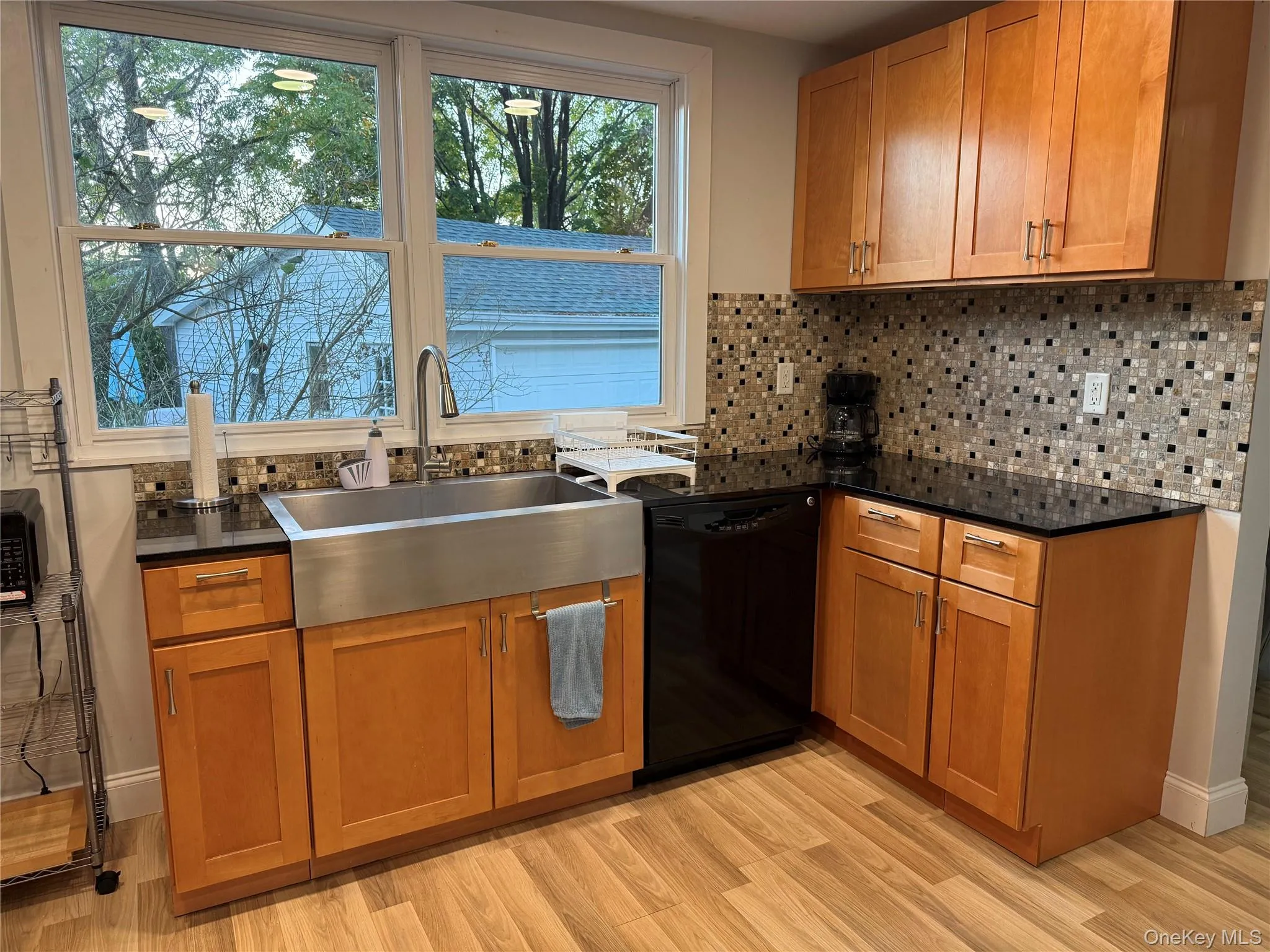 Kitchen with brown cabinets, decorative backsplash, black dishwasher, and light wood-style floors Kitchen with brown cabinets, decorative backsplash, black dishwasher, and light wood-style floors