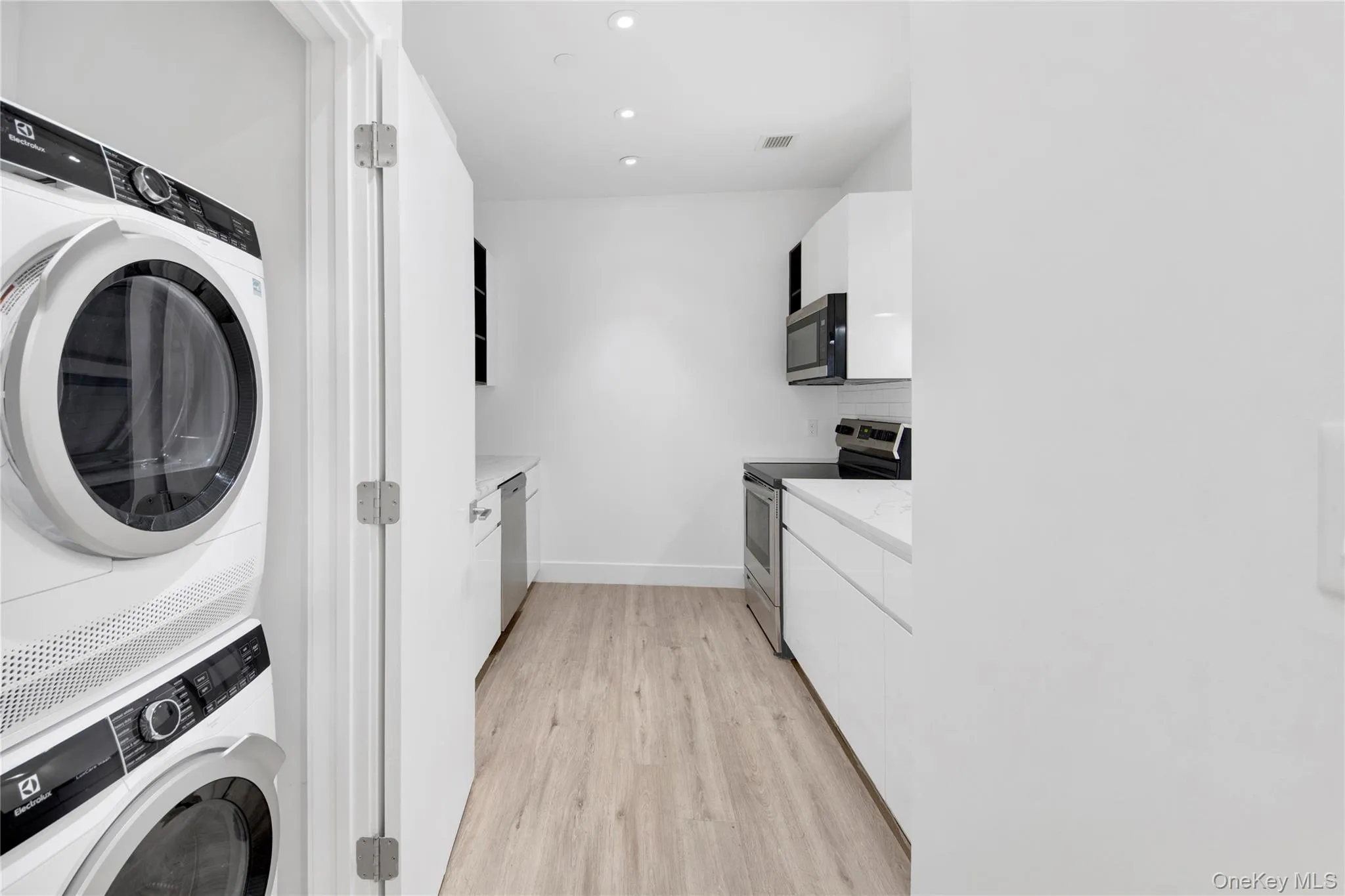 Washroom featuring light wood finished floors, stacked washing machine and dryer, and recessed lighting Washroom featuring light wood finished floors, stacked washing machine and dryer, and recessed lighting