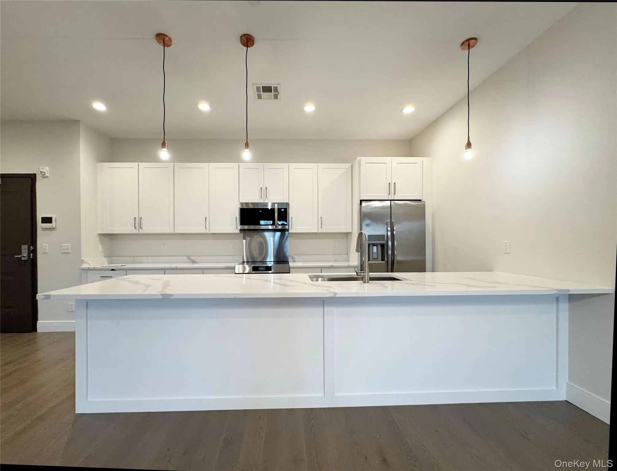 Kitchen with white cabinetry, a peninsula, dark wood-style flooring, appliances with stainless steel finishes, and recessed lighting Kitchen with white cabinetry, a peninsula, dark wood-style flooring, appliances with stainless steel finishes, and recessed lighting