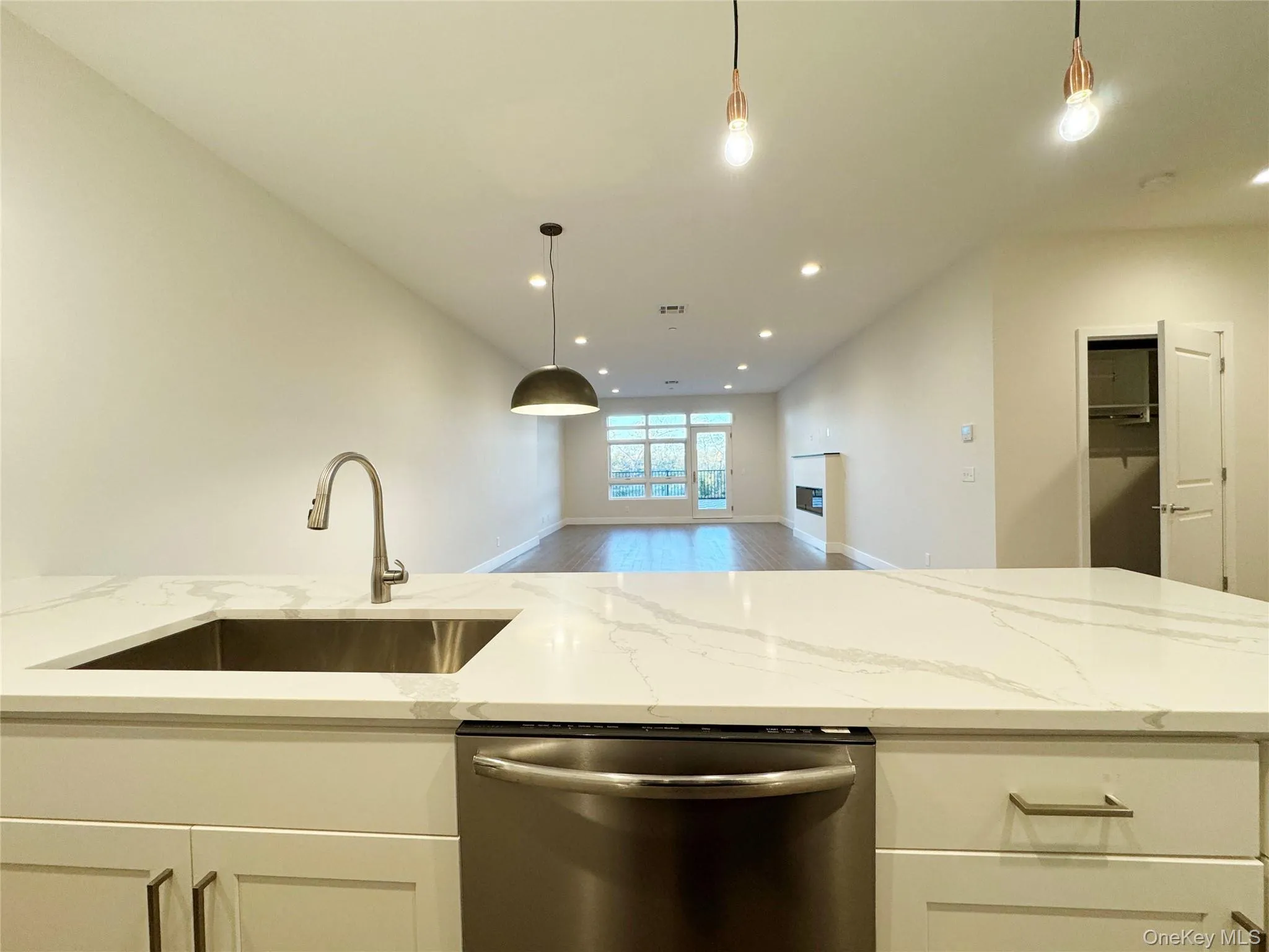 Kitchen with light stone counters, decorative light fixtures, stainless steel dishwasher, white cabinetry, and recessed lighting Kitchen with light stone counters, decorative light fixtures, stainless steel dishwasher, white cabinetry, and recessed lighting