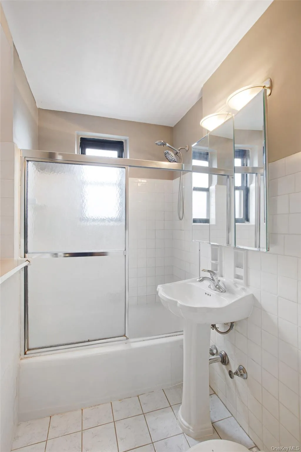 Full bathroom with bath / shower combo with glass door, healthy amount of natural light, light tile patterned floors, and tile walls Full bathroom with bath / shower combo with glass door, healthy amount of natural light, light tile patterned floors, and tile walls