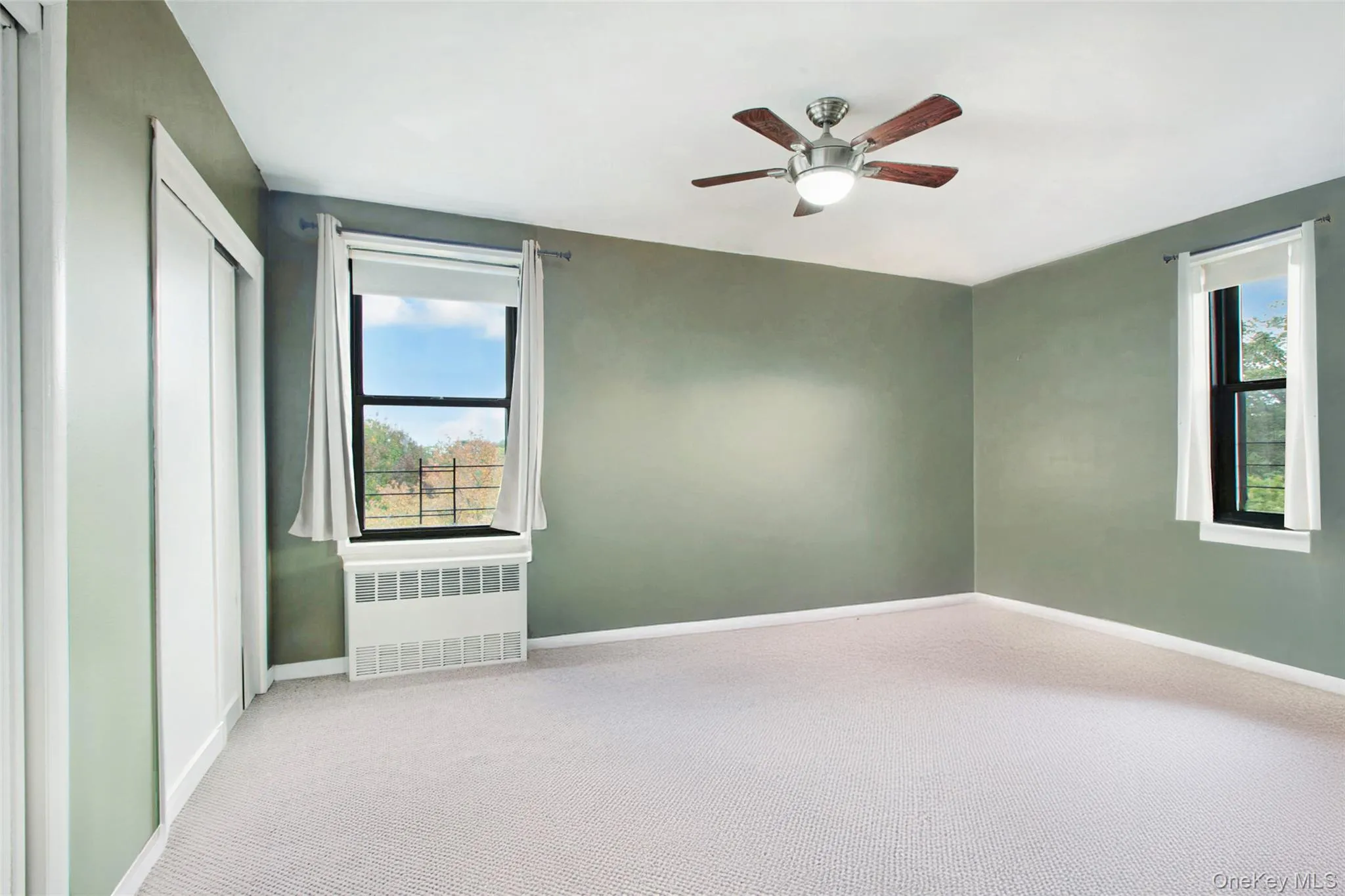 Unfurnished bedroom featuring radiator, ceiling fan, carpet flooring, and multiple windows Unfurnished bedroom featuring radiator, ceiling fan, carpet flooring, and multiple windows