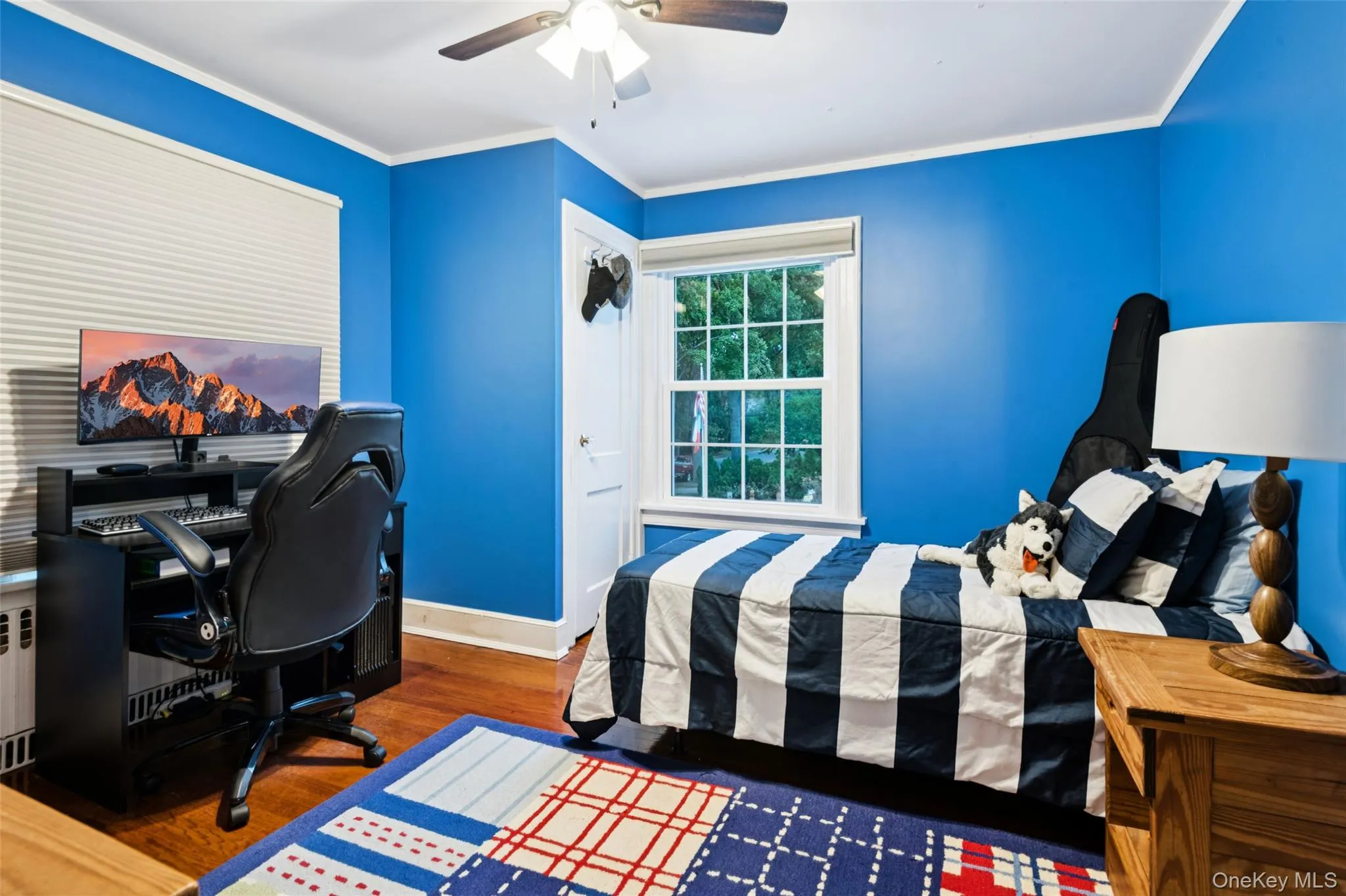 Bedroom featuring dark wood-style floors, ornamental molding, an office area, a ceiling fan, and radiator Bedroom featuring dark wood-style floors, ornamental molding, an office area, a ceiling fan, and radiator