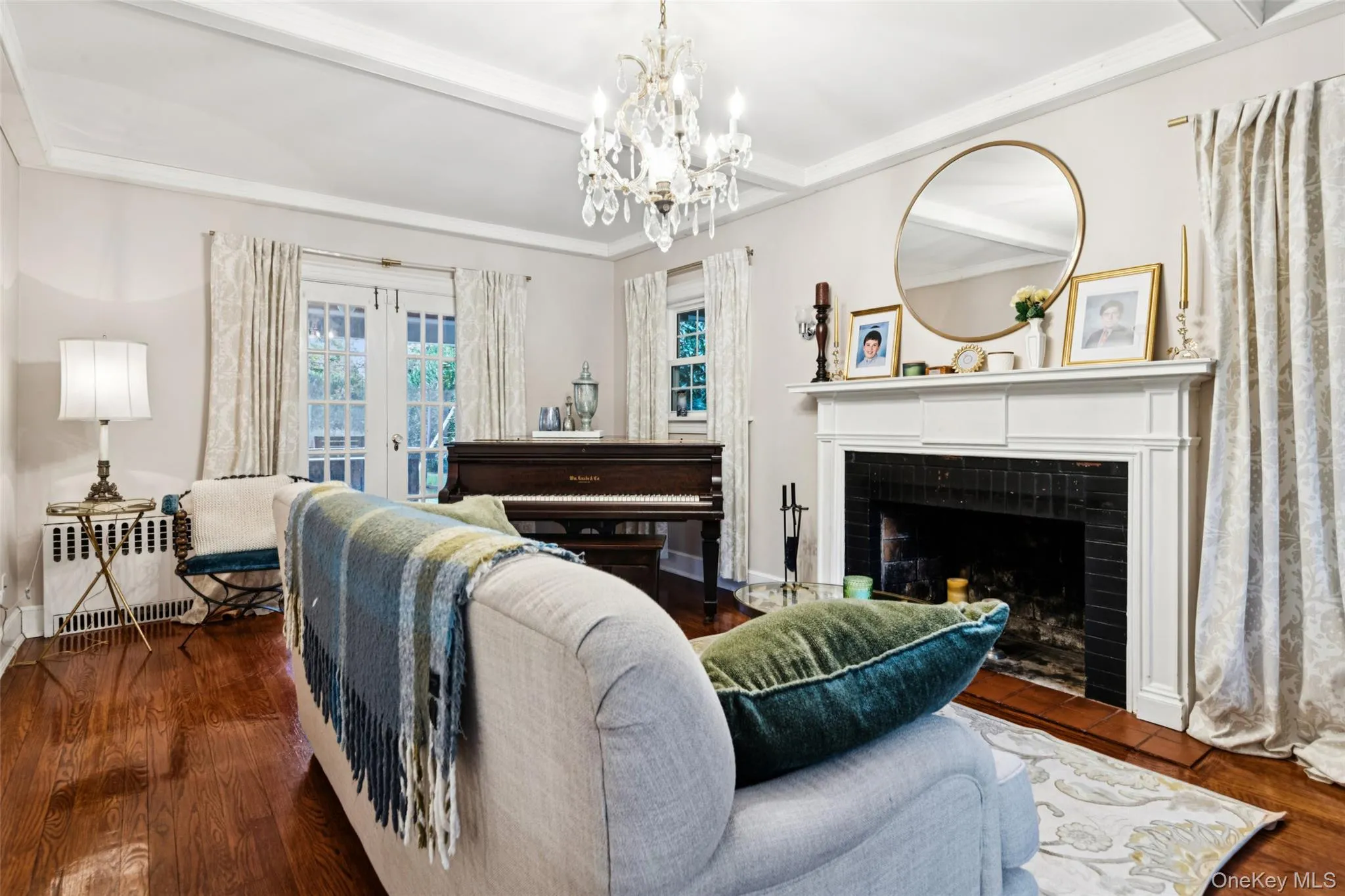 Living room with radiator, a fireplace, dark wood-style flooring, a chandelier, and french doors Living room with radiator, a fireplace, dark wood-style flooring, a chandelier, and french doors