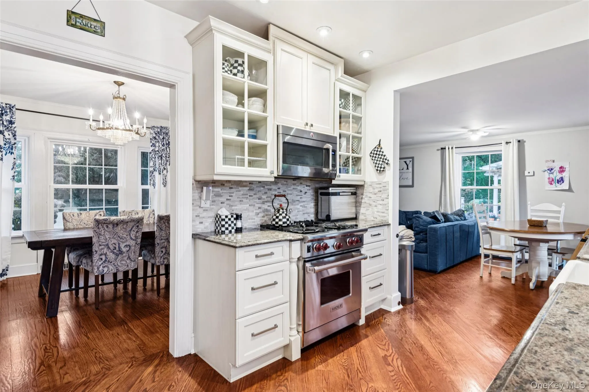 Kitchen with glass insert cabinets, appliances with stainless steel finishes, light stone counters, white cabinets, and decorative backsplash Kitchen with glass insert cabinets, appliances with stainless steel finishes, light stone counters, white cabinets, and decorative backsplash