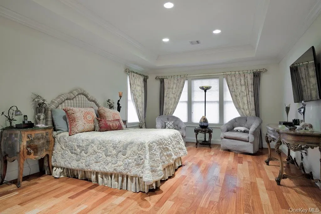 Bedroom with a raised ceiling, ornamental molding, light wood-type flooring, and recessed lighting Bedroom with a raised ceiling, ornamental molding, light wood-type flooring, and recessed lighting