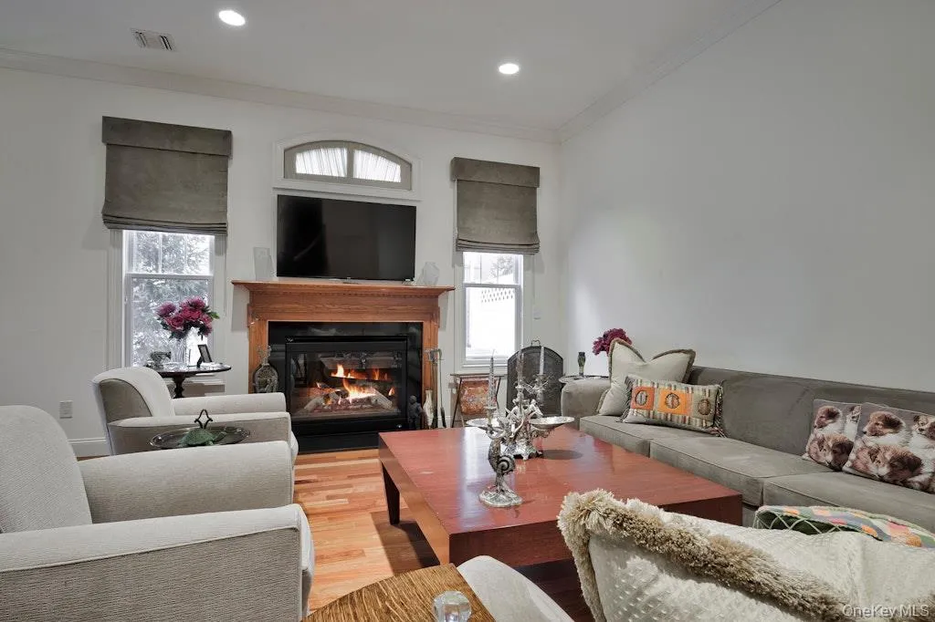 Living area featuring wood finished floors, ornamental molding, a glass covered fireplace, and recessed lighting Living area featuring wood finished floors, ornamental molding, a glass covered fireplace, and recessed lighting
