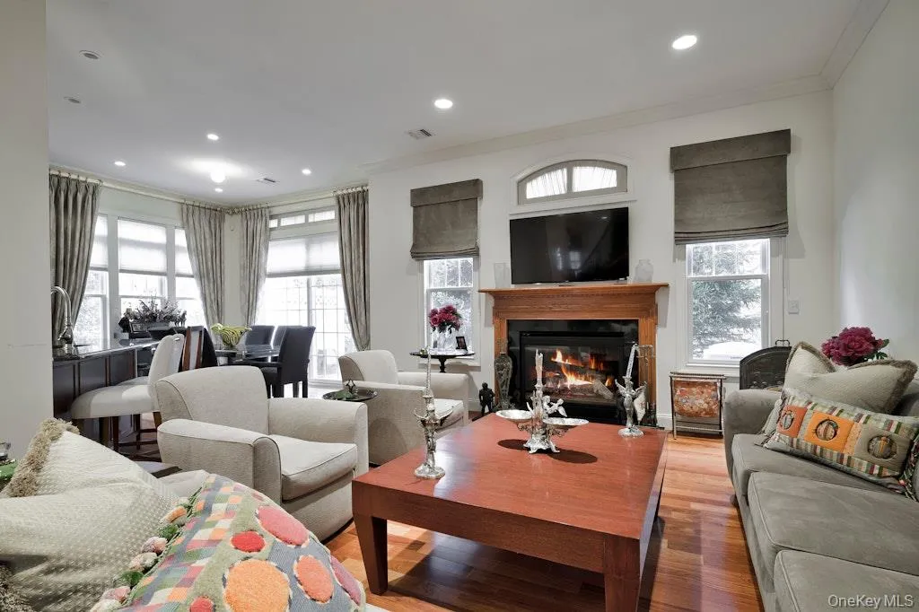 Living room with wood finished floors, a glass covered fireplace, ornamental molding, and recessed lighting Living room with wood finished floors, a glass covered fireplace, ornamental molding, and recessed lighting