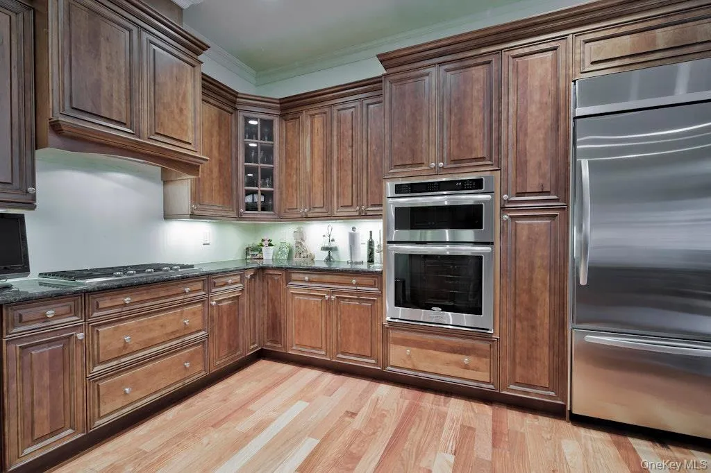 Kitchen featuring stainless steel appliances, glass insert cabinets, light wood finished floors, dark stone countertops, and crown molding Kitchen featuring stainless steel appliances, glass insert cabinets, light wood finished floors, dark stone countertops, and crown molding