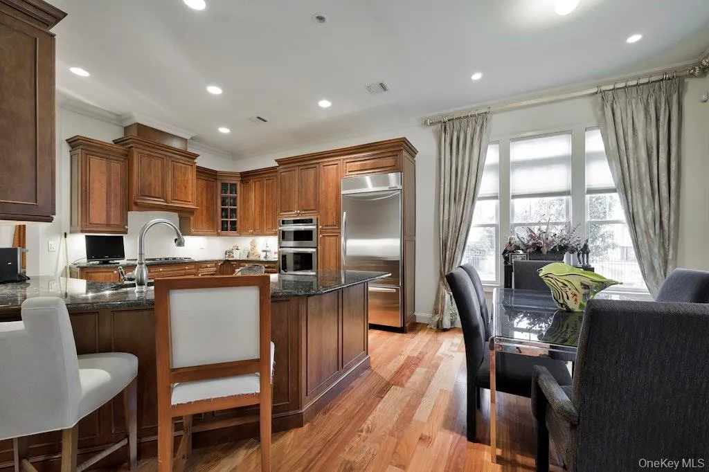 Kitchen with dark stone counters, stainless steel appliances, a breakfast bar area, light wood finished floors, and recessed lighting Kitchen with dark stone counters, stainless steel appliances, a breakfast bar area, light wood finished floors, and recessed lighting