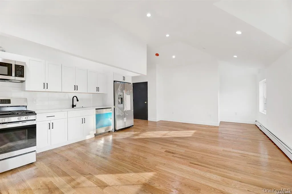 Kitchen with stainless steel appliances, white cabinetry, light wood-type flooring, tasteful backsplash, and high vaulted ceiling Kitchen with stainless steel appliances, white cabinetry, light wood-type flooring, tasteful backsplash, and high vaulted ceiling