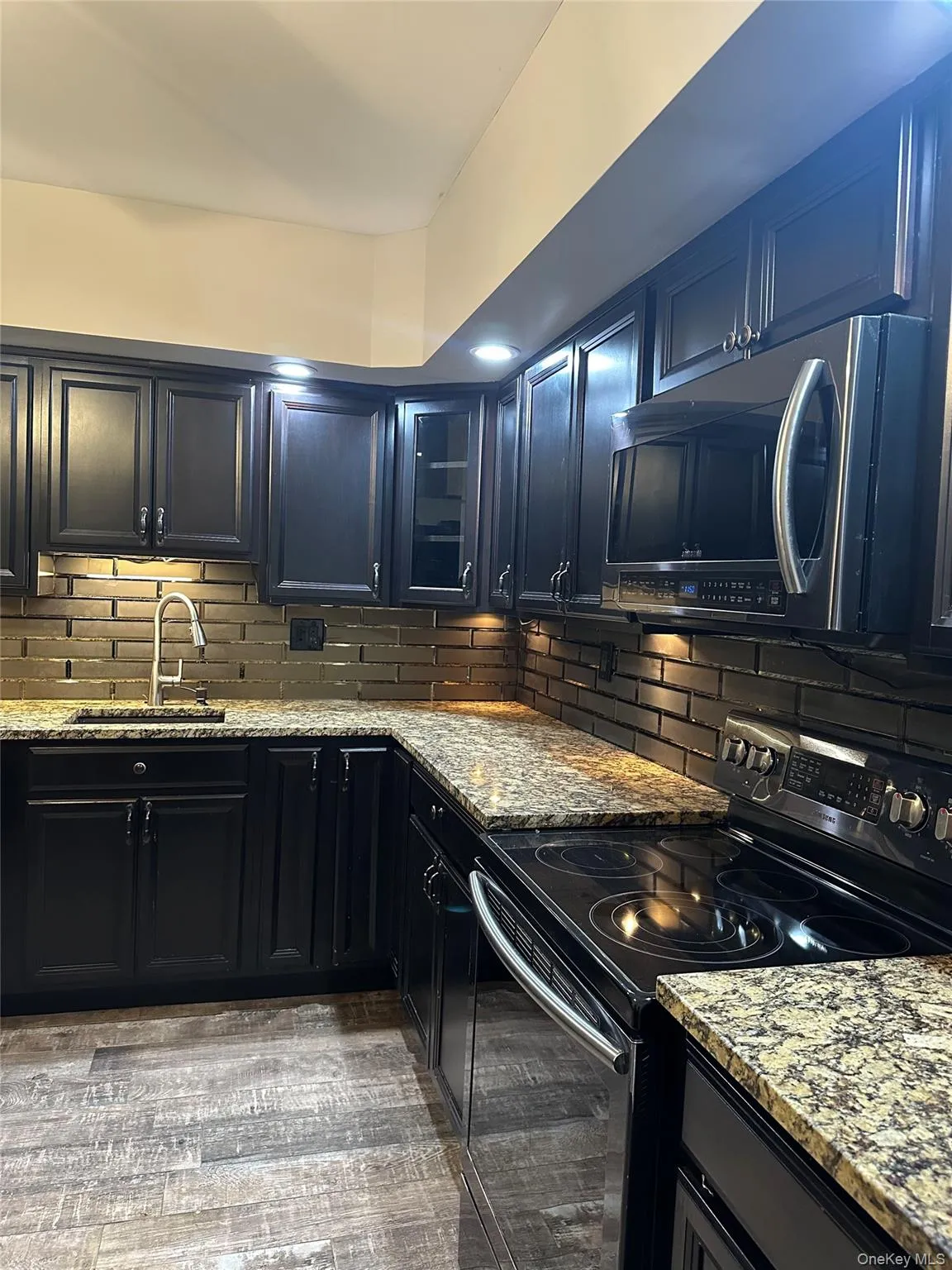 Kitchen featuring black range with electric cooktop, dark cabinets, light stone counters, and backsplash Kitchen featuring black range with electric cooktop, dark cabinets, light stone counters, and backsplash