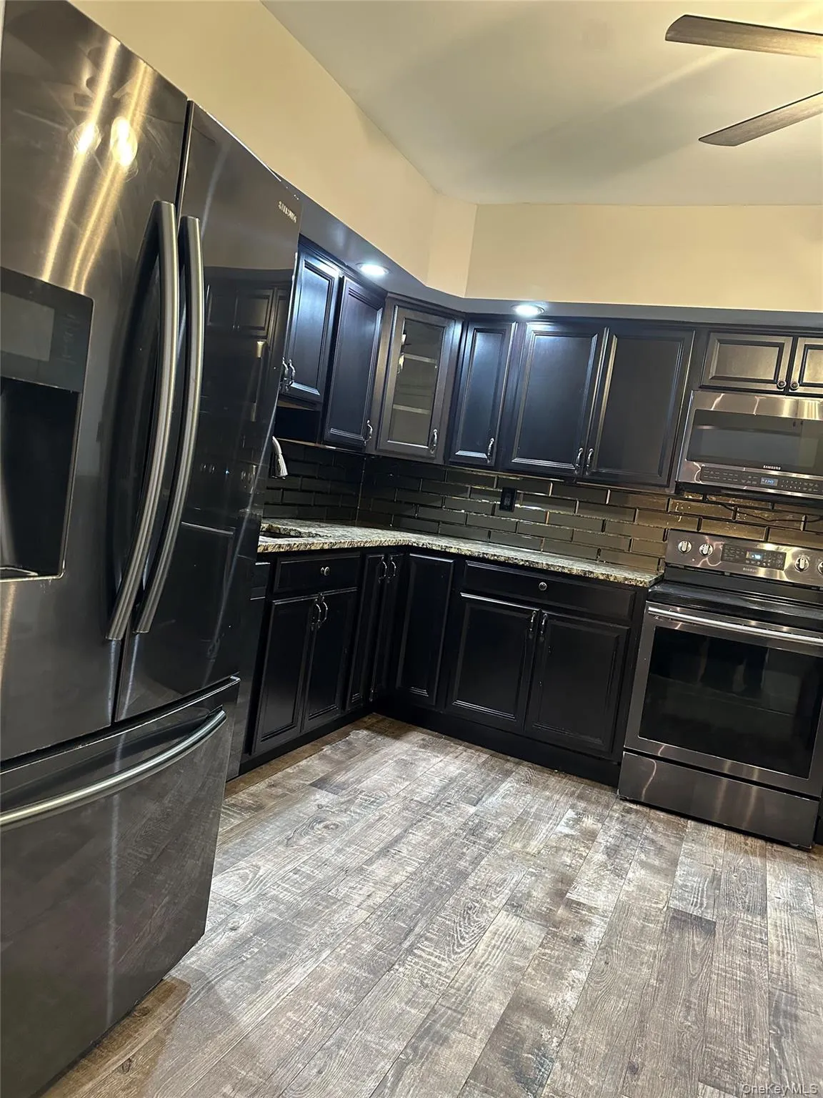 Kitchen with dark cabinetry, appliances with stainless steel finishes, and backsplash Kitchen with dark cabinetry, appliances with stainless steel finishes, and backsplash