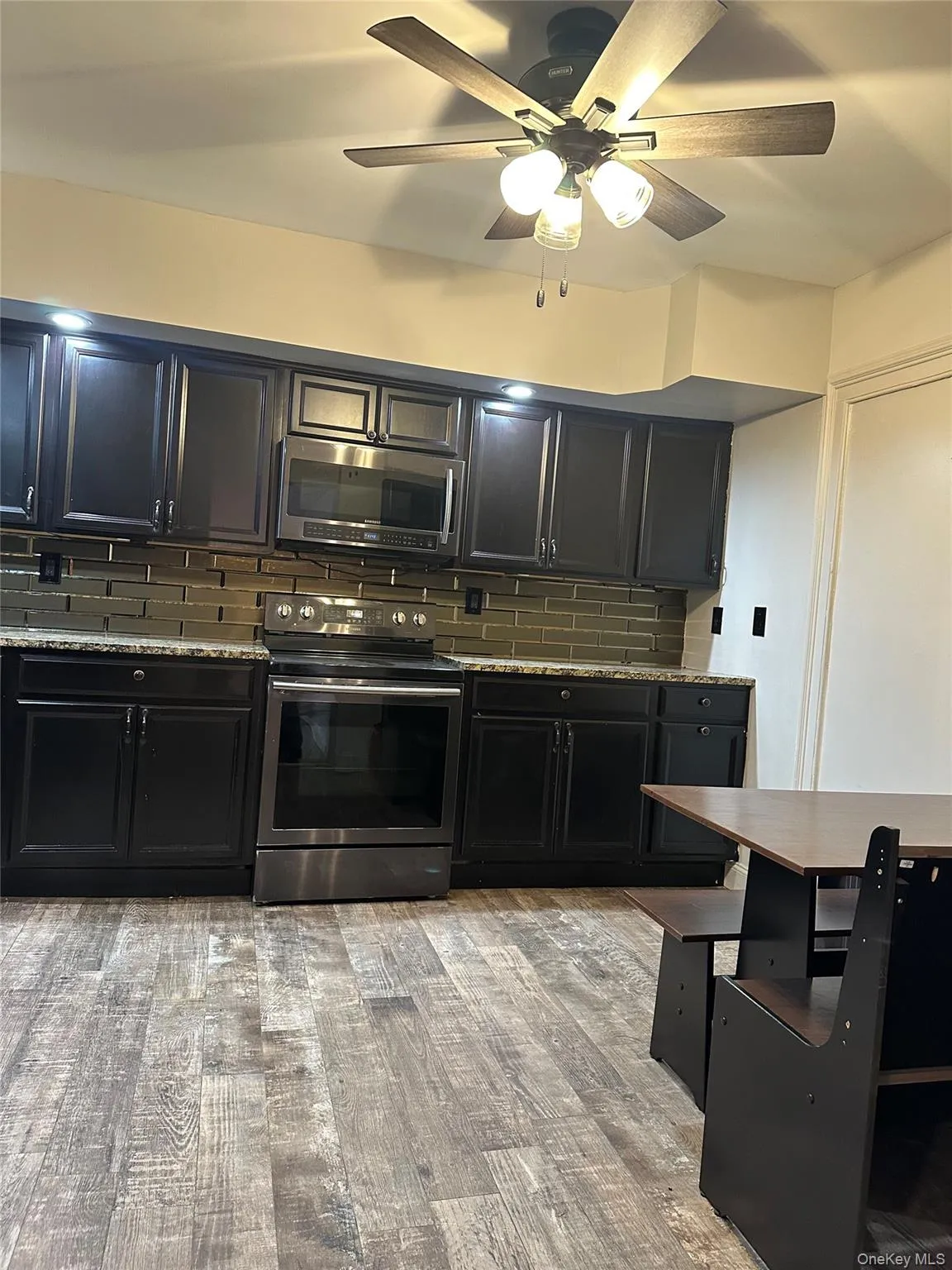 Kitchen featuring decorative backsplash, appliances with stainless steel finishes, dark cabinetry, ceiling fan, and light wood-style floors Kitchen featuring decorative backsplash, appliances with stainless steel finishes, dark cabinetry, ceiling fan, and light wood-style floors