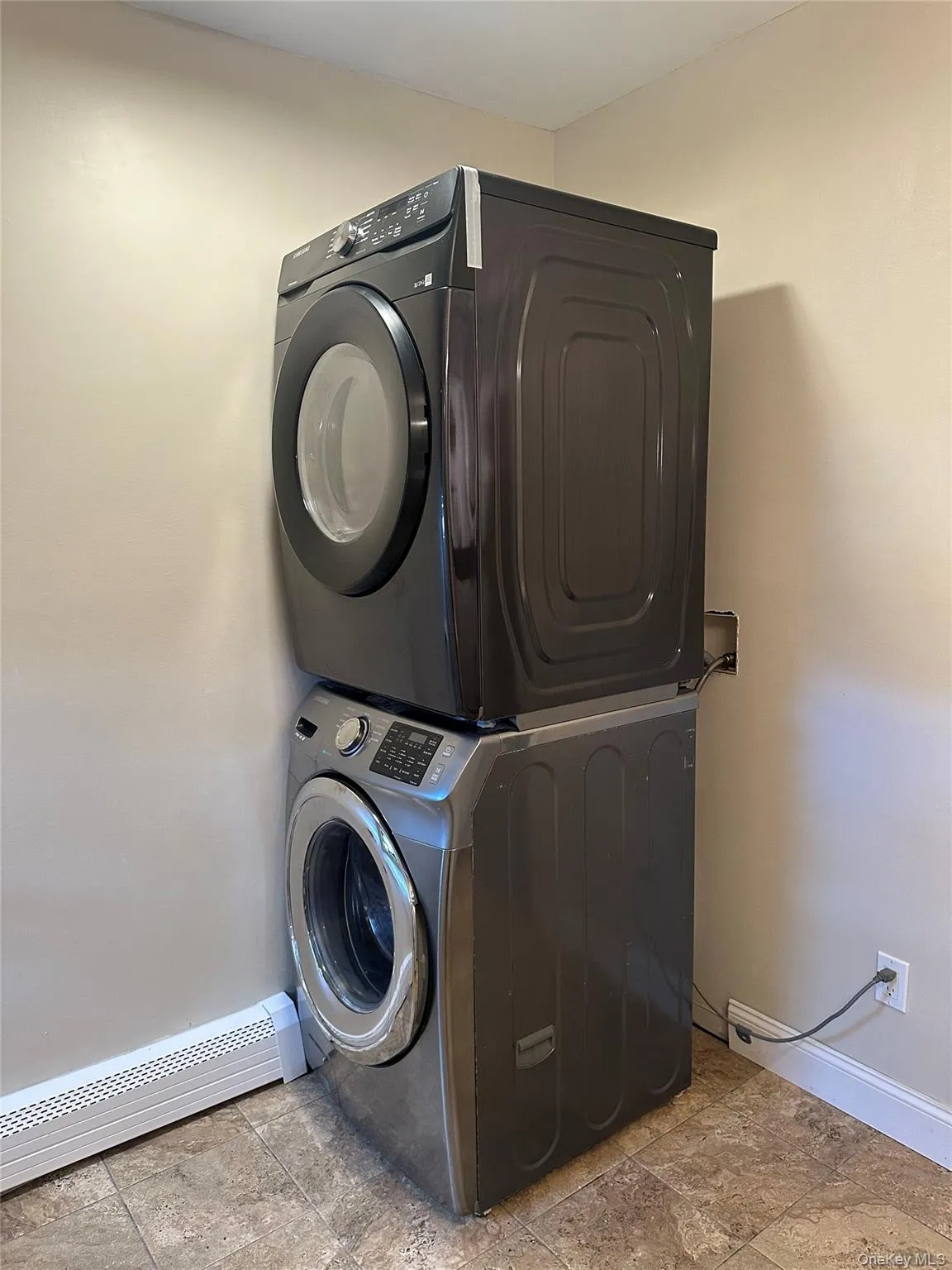 Washroom with stacked washing machine and dryer and a baseboard heating unit Washroom with stacked washing machine and dryer and a baseboard heating unit