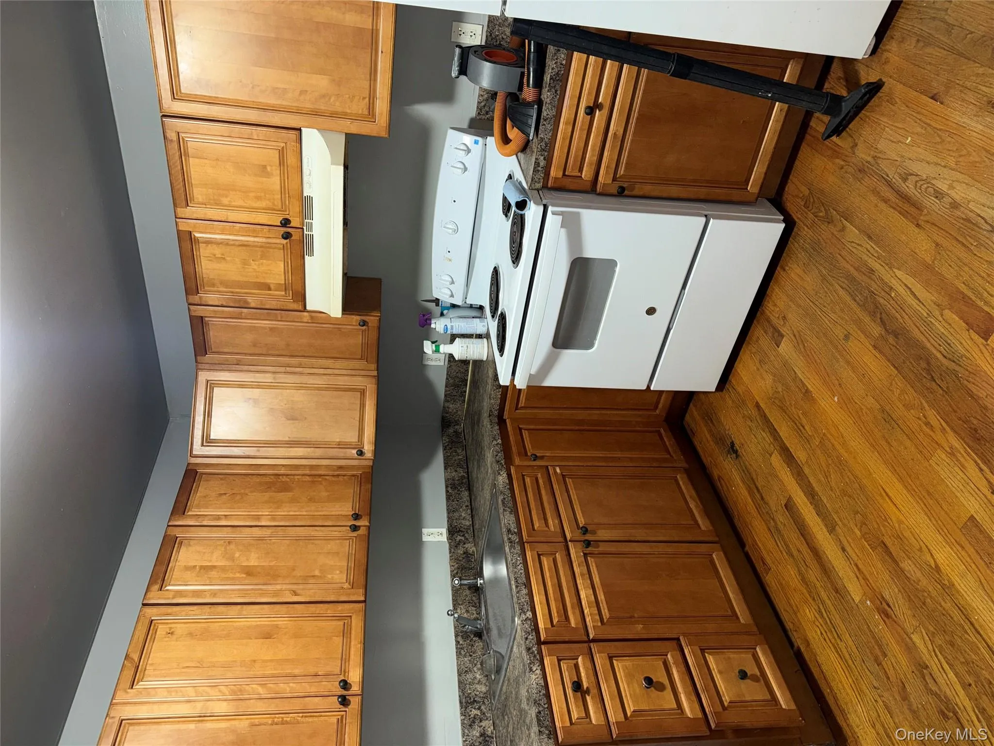 Kitchen featuring electric range, dark countertops, dark wood-style flooring, and brown cabinetry Kitchen featuring electric range, dark countertops, dark wood-style flooring, and brown cabinetry