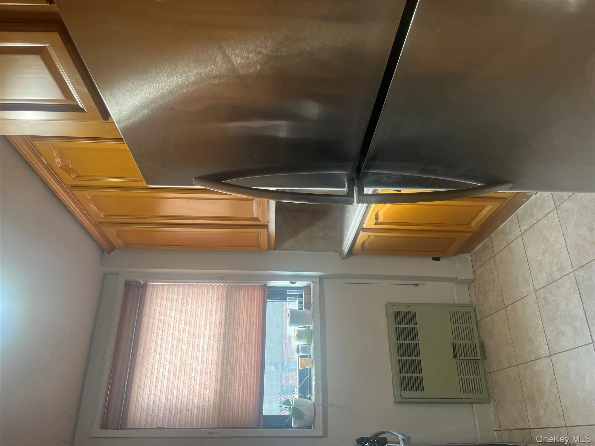 Kitchen featuring stainless steel fridge, radiator heating unit, light countertops, light tile patterned floors, and brown cabinets Kitchen featuring stainless steel fridge, radiator heating unit, light countertops, light tile patterned floors, and brown cabinets