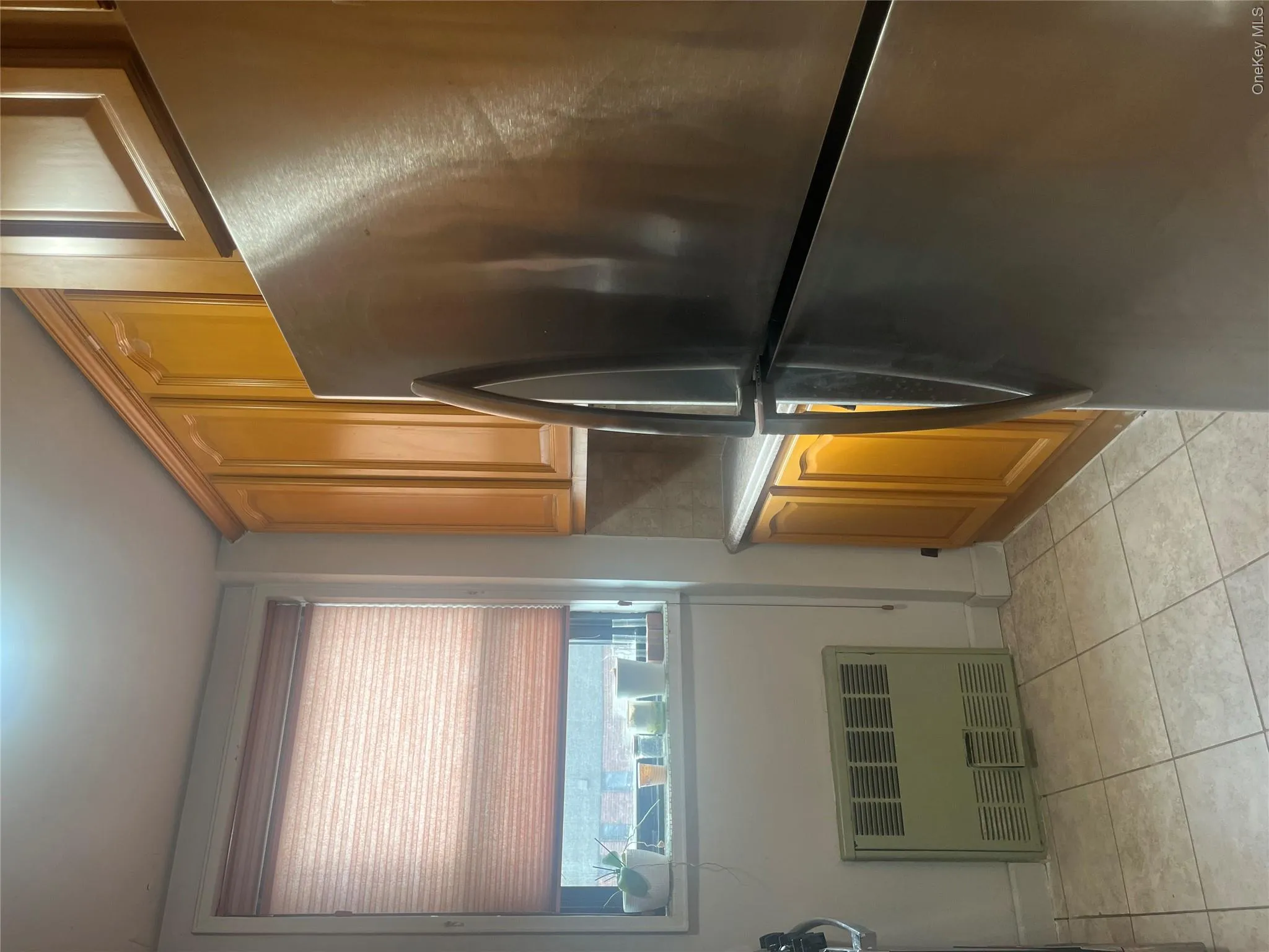 Kitchen featuring stainless steel fridge, radiator heating unit, light countertops, light tile patterned floors, and brown cabinets Kitchen featuring stainless steel fridge, radiator heating unit, light countertops, light tile patterned floors, and brown cabinets