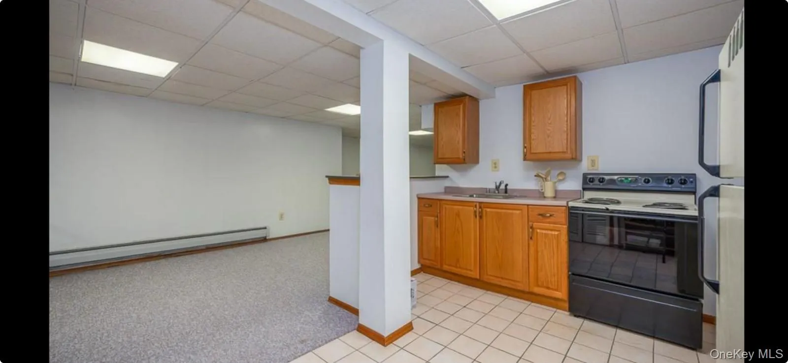 Kitchen with electric range, light countertops, a baseboard radiator, freestanding refrigerator, and a drop ceiling Kitchen with electric range, light countertops, a baseboard radiator, freestanding refrigerator, and a drop ceiling