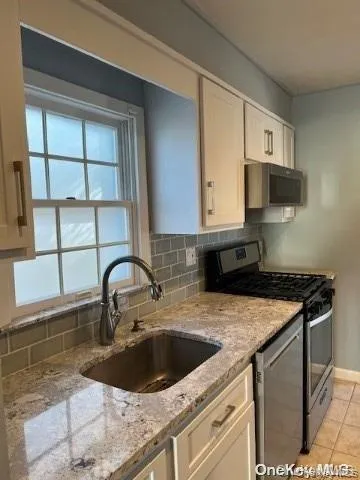 Kitchen with appliances with stainless steel finishes, tasteful backsplash, light stone countertops, and light tile patterned flooring Kitchen with appliances with stainless steel finishes, tasteful backsplash, light stone countertops, and light tile patterned flooring