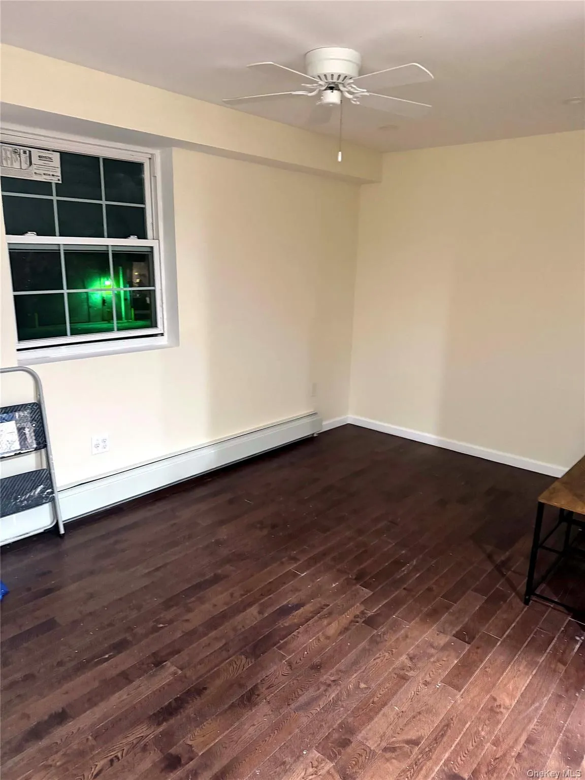Unfurnished room featuring dark wood-style flooring, a baseboard heating unit, and ceiling fan Unfurnished room featuring dark wood-style flooring, a baseboard heating unit, and ceiling fan