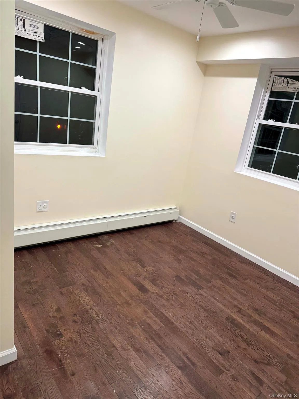 Empty room with dark wood-style floors, a baseboard radiator, and a ceiling fan Empty room with dark wood-style floors, a baseboard radiator, and a ceiling fan