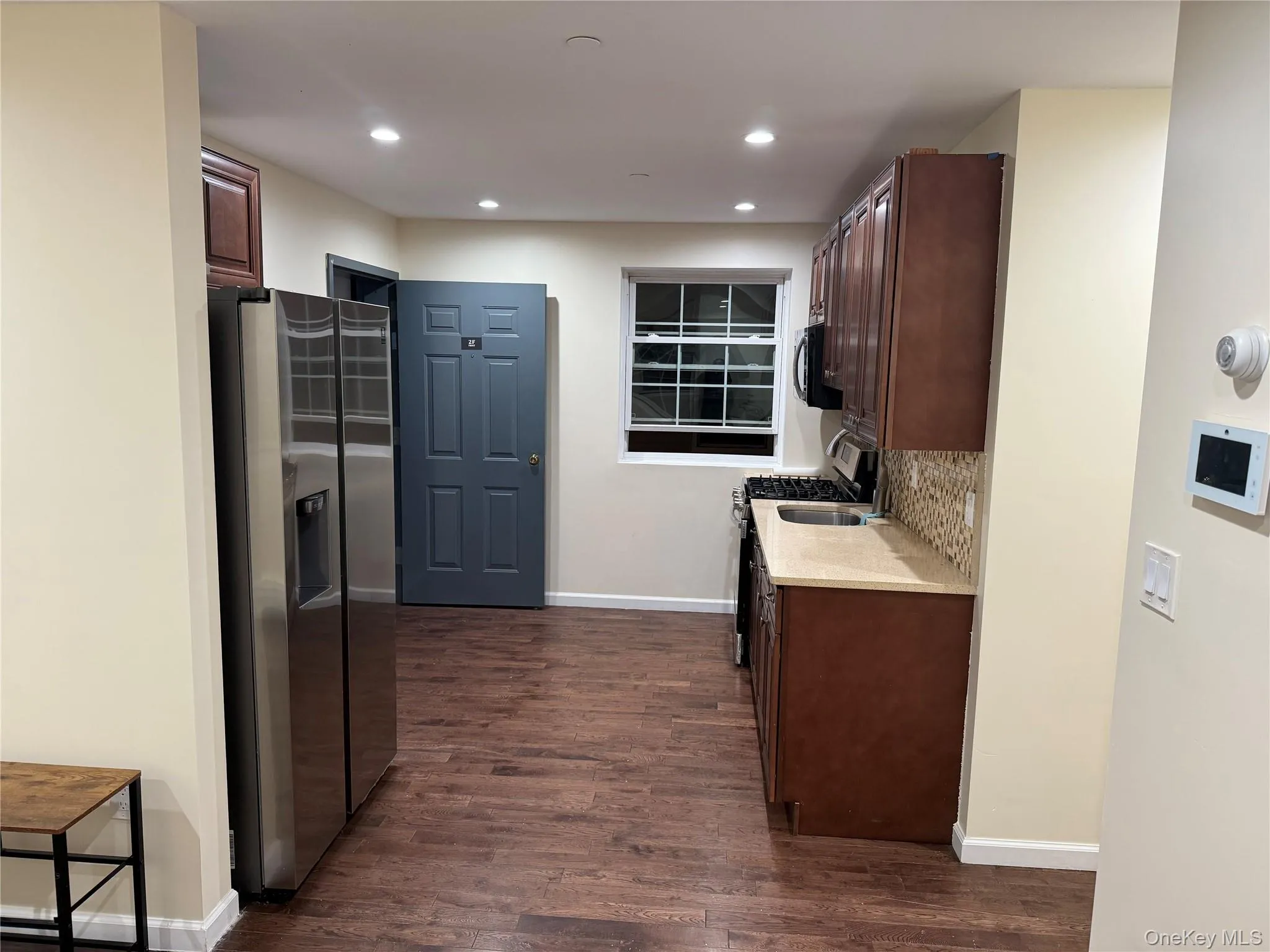 Kitchen featuring stainless steel appliances, dark wood finished floors, light stone counters, backsplash, and dark brown cabinets Kitchen featuring stainless steel appliances, dark wood finished floors, light stone counters, backsplash, and dark brown cabinets