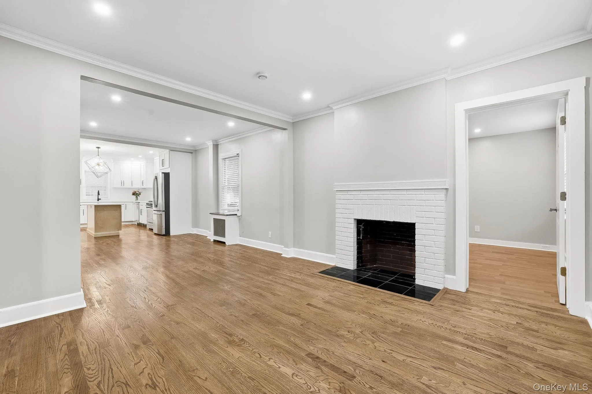 Unfurnished living room featuring light wood-type flooring, ornamental molding, a brick fireplace, recessed lighting, and radiator Unfurnished living room featuring light wood-type flooring, ornamental molding, a brick fireplace, recessed lighting, and radiator