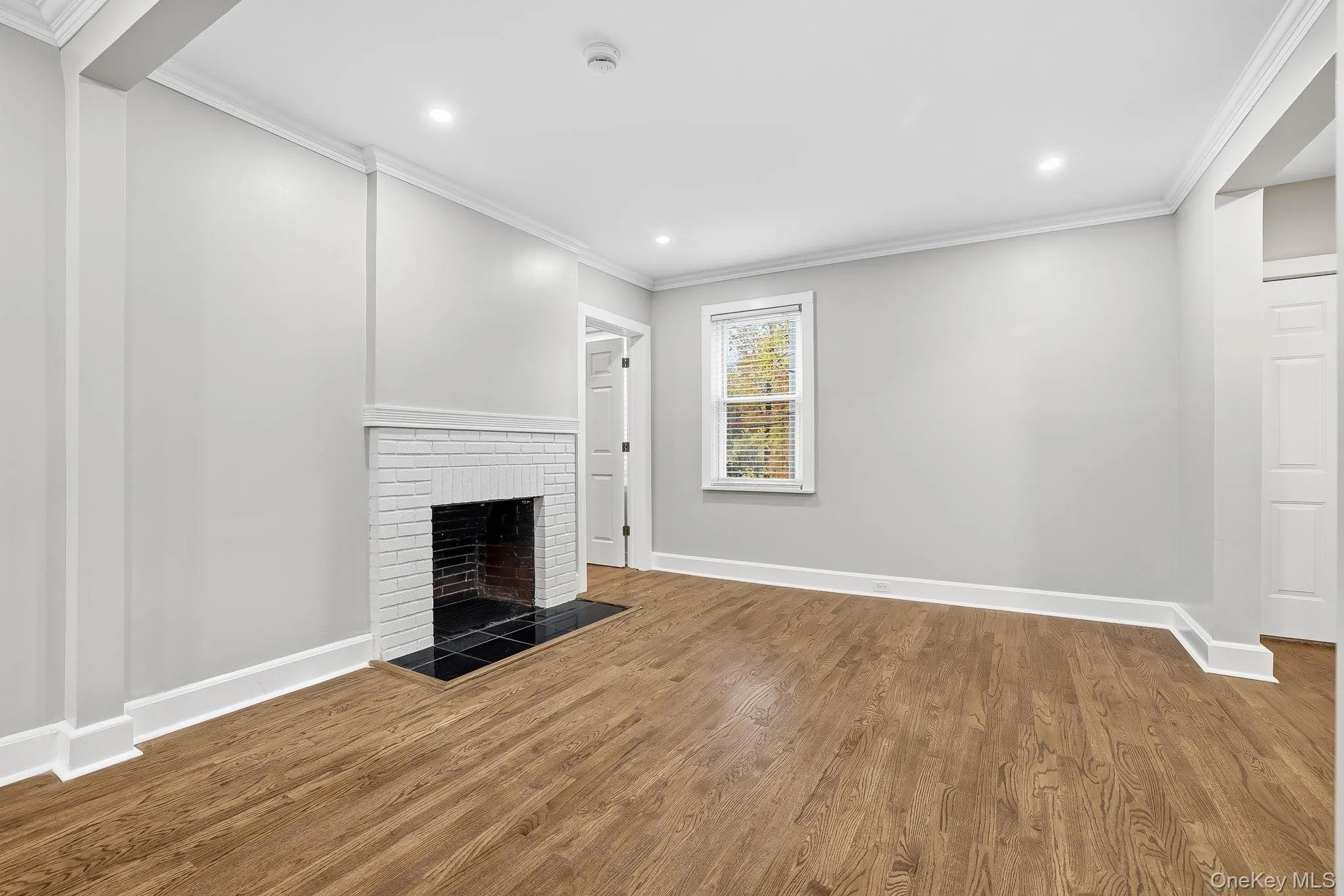 Unfurnished living room with ornamental molding, wood finished floors, a brick fireplace, and recessed lighting Unfurnished living room with ornamental molding, wood finished floors, a brick fireplace, and recessed lighting