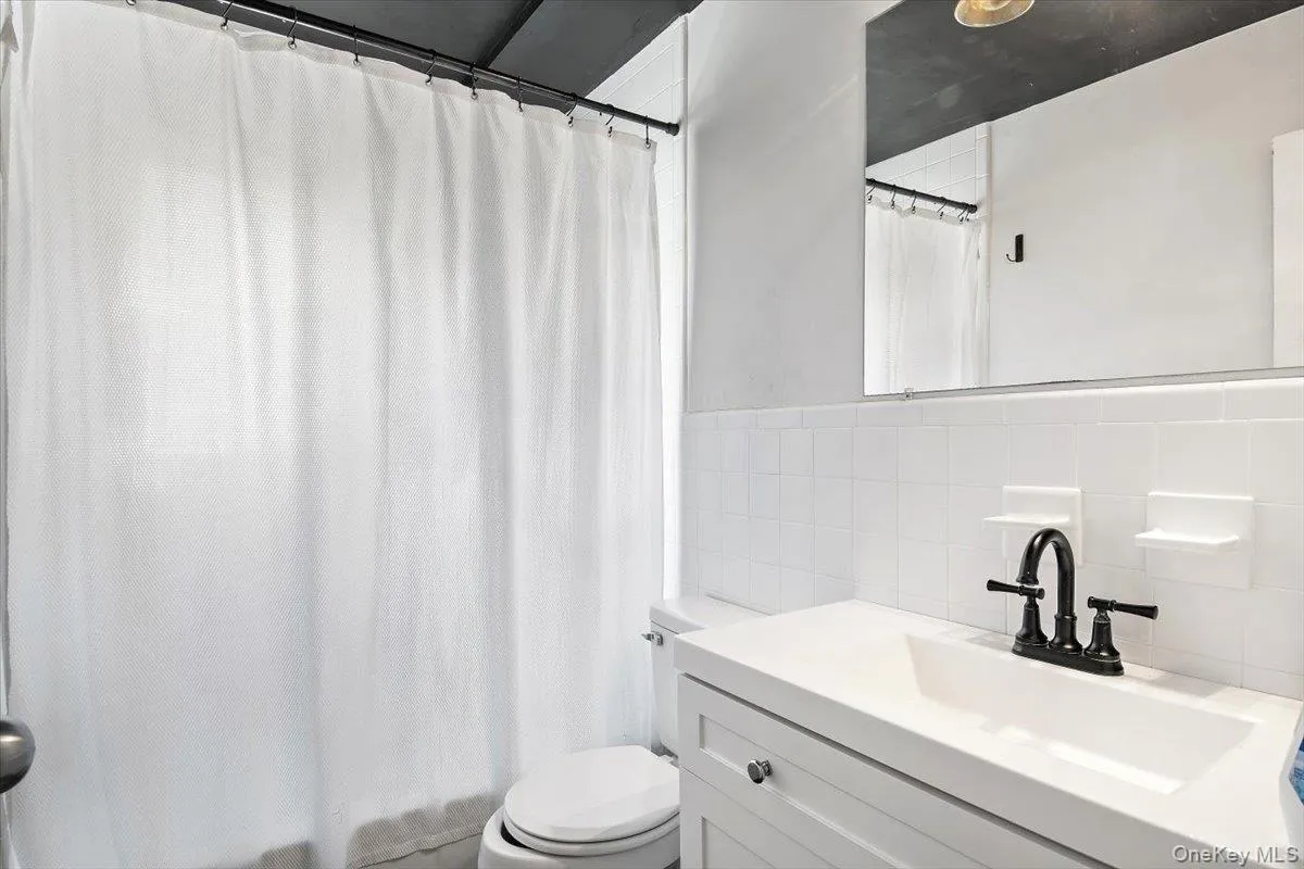 Full bathroom with vanity, a shower with curtain, tile walls, and backsplash Full bathroom with vanity, a shower with curtain, tile walls, and backsplash