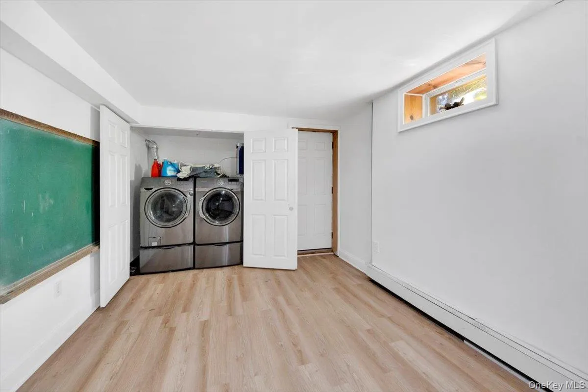 Laundry area featuring baseboard heating, wood finished floors, and washing machine and clothes dryer Laundry area featuring baseboard heating, wood finished floors, and washing machine and clothes dryer